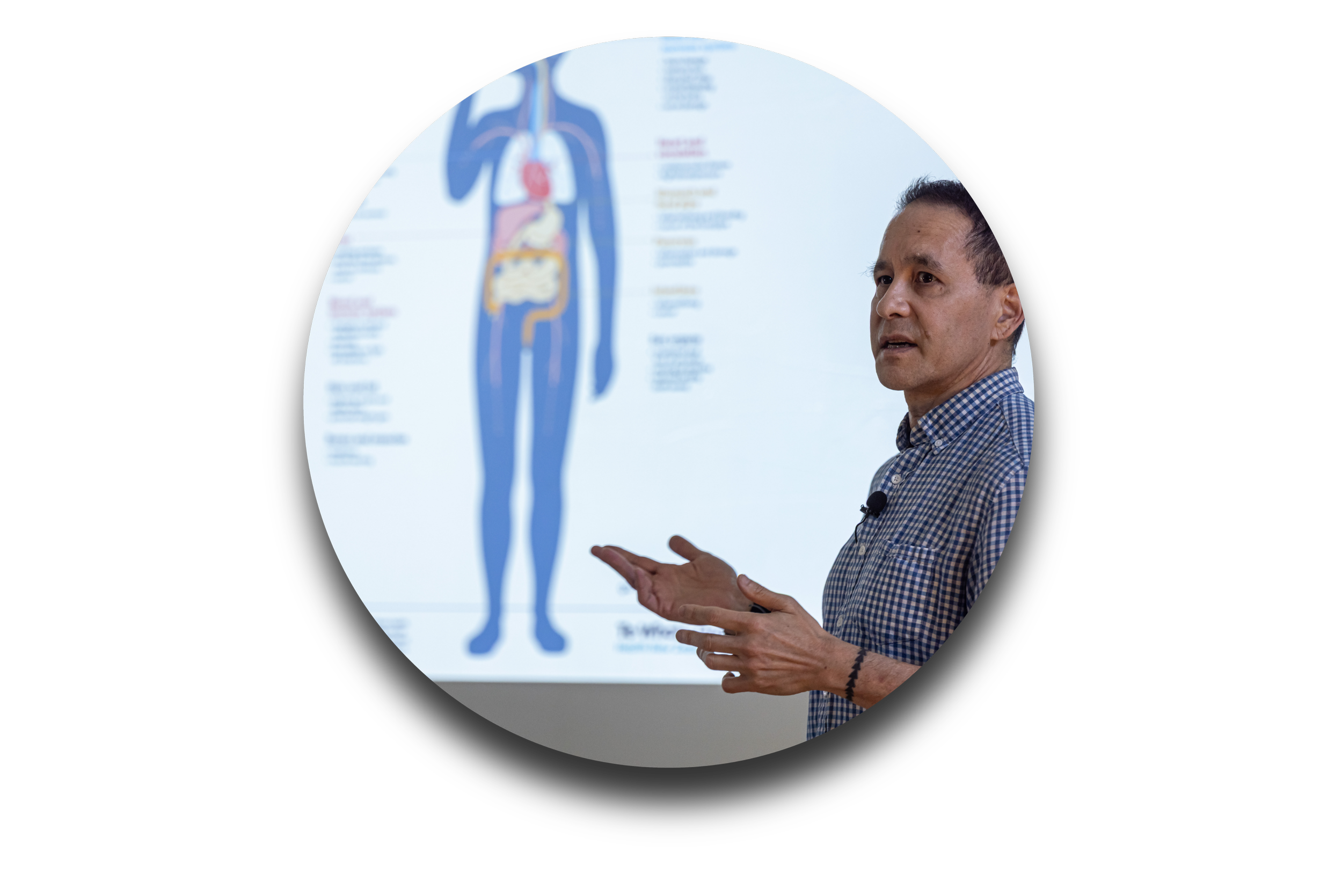 A man in a checkered shirt giving a presentation about human anatomy, standing in front of a diagram of the human body.
