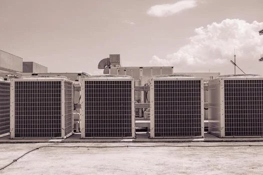 Four large industrial air conditioning units on a building rooftop with a cloudy sky
