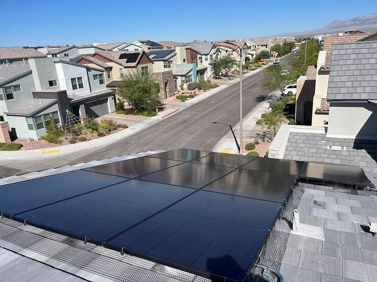 View of a residential neighborhood with houses, a street, and a solar panel installation on the roof in the foreground.