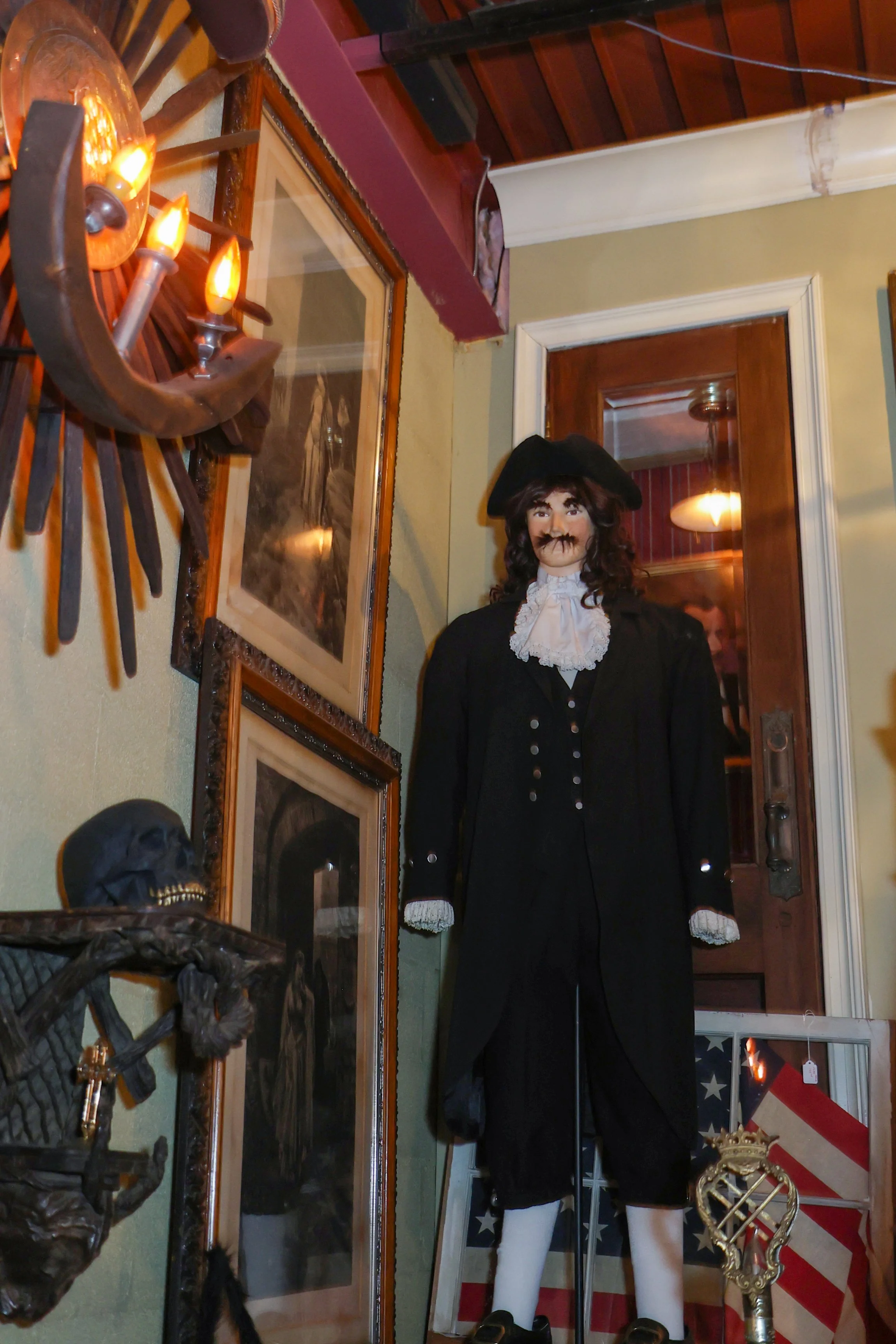A wax figure dressed as a colonial-era soldier or officer stands in a room with Americana decorations, including an American flag and other patriotic items, and is surrounded by various artifacts and decorations.