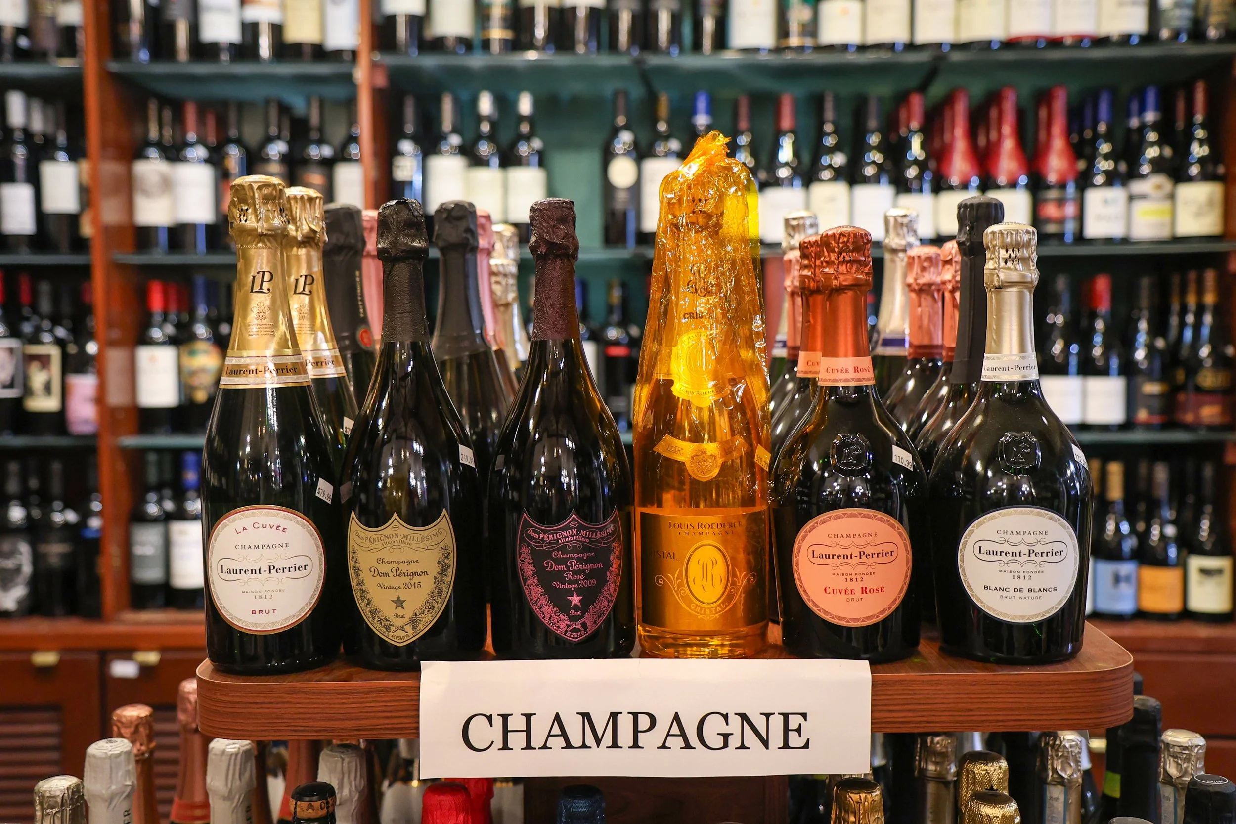 Display of various bottles of champagne on a wooden shelf with a sign labeled 'Champagne' in front of them.