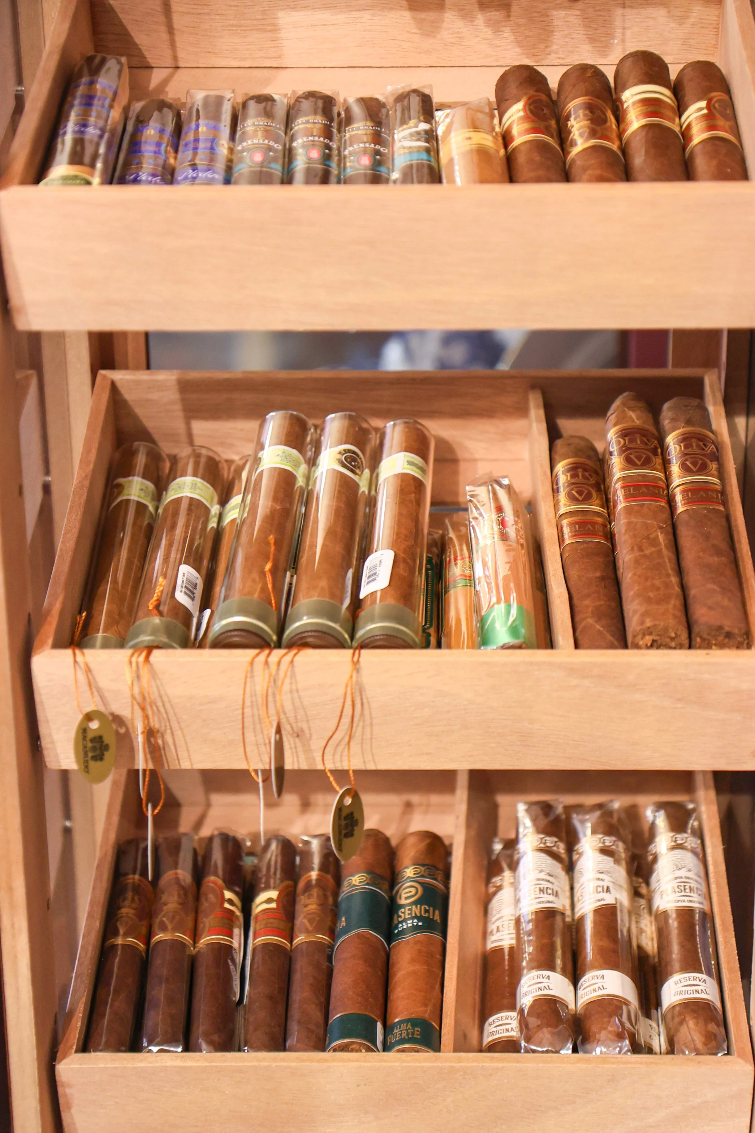 A wooden display case containing multiple rows of cigars, each with various colorful labels.