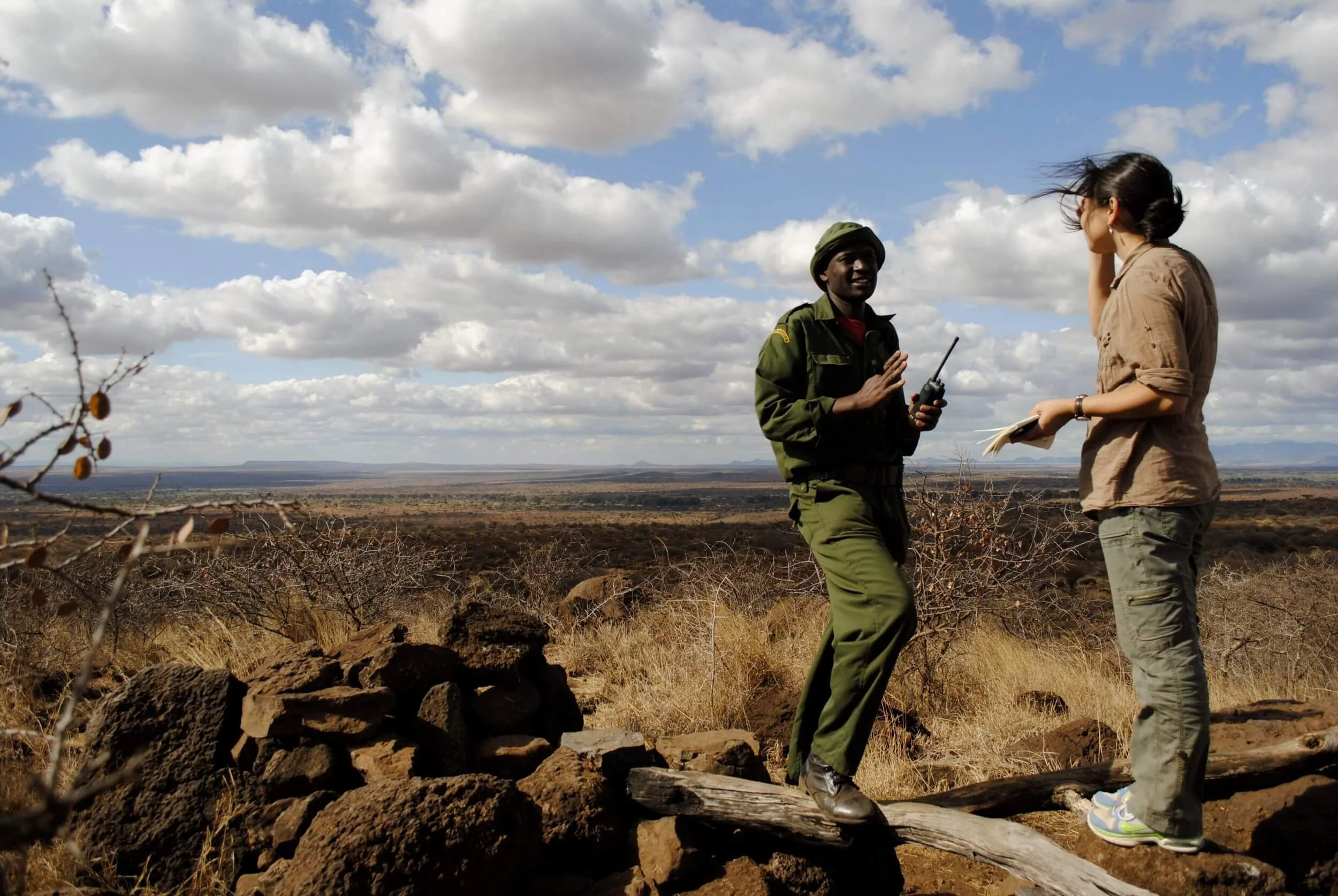 Asian woman talks to African wildlife ranger with Kenyan landscape behind them