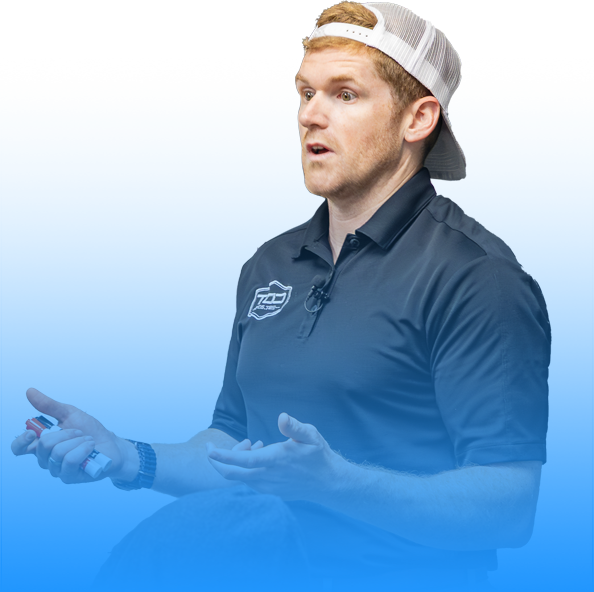 Man in navy polo shirt and white backward cap speaking on a blue background.