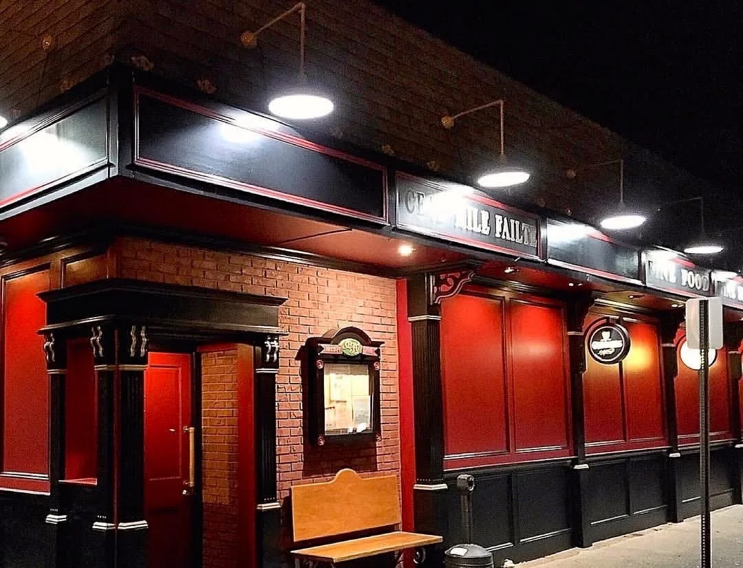 Exterior of a pub or bar with red and black decor, a brick wall, and illuminated signage.