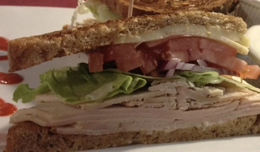 Close-up of a turkey sandwich with lettuce, tomato, red onion, cheese, and toasted bread.