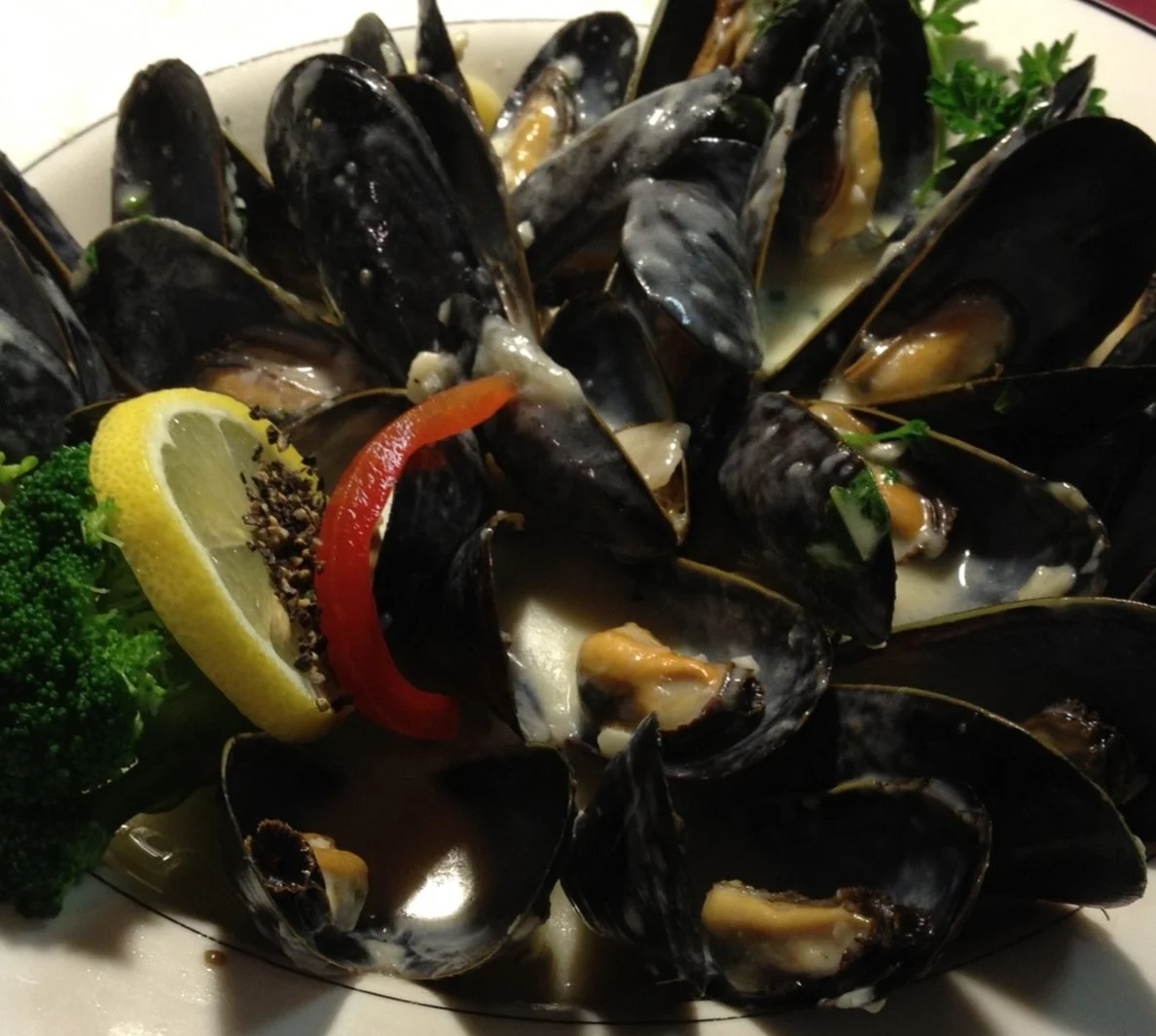 A plate of cooked mussels garnished with lemon, red bell pepper, and parsley.