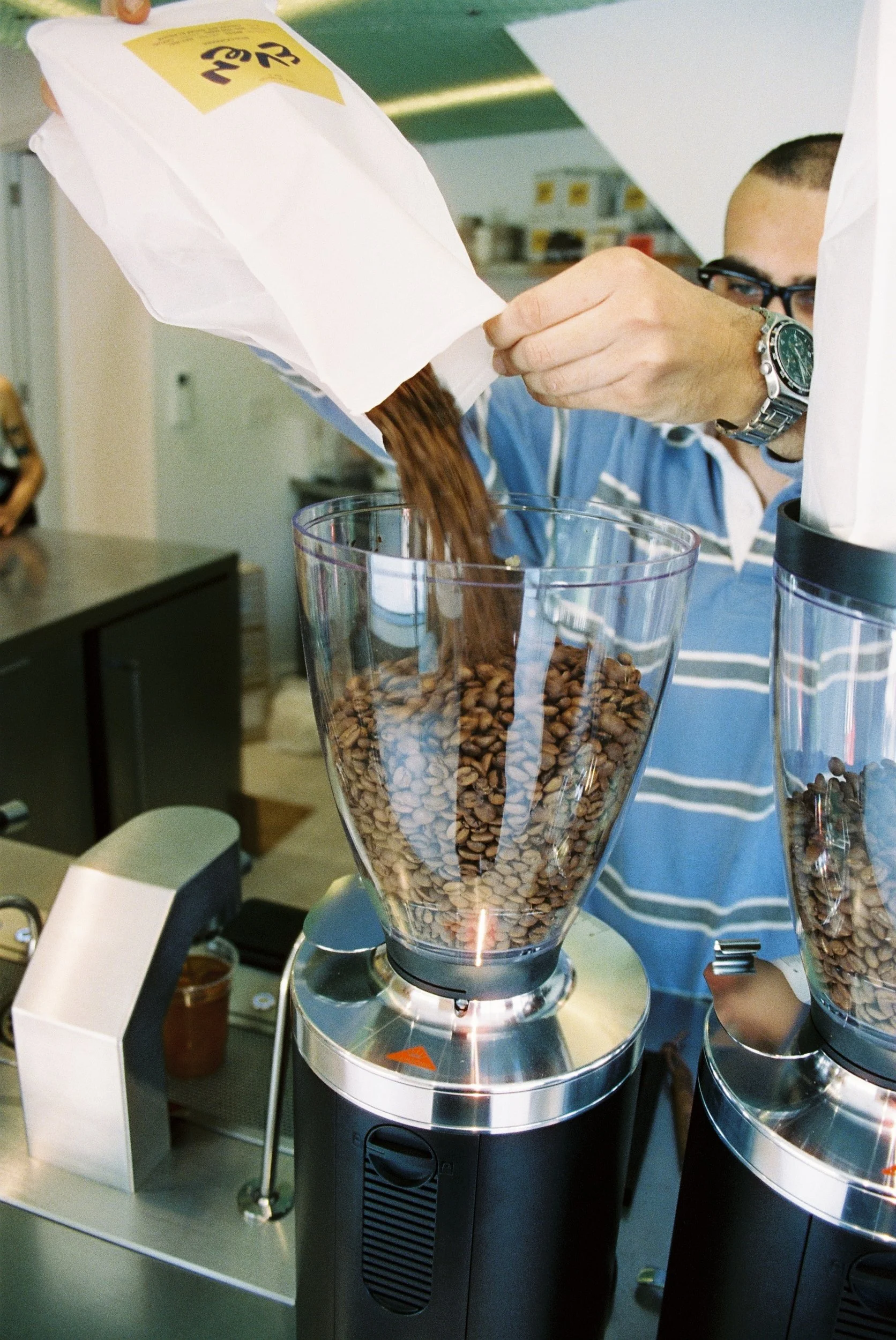 Person pouring coffee beans into a coffee grinder at a store display.