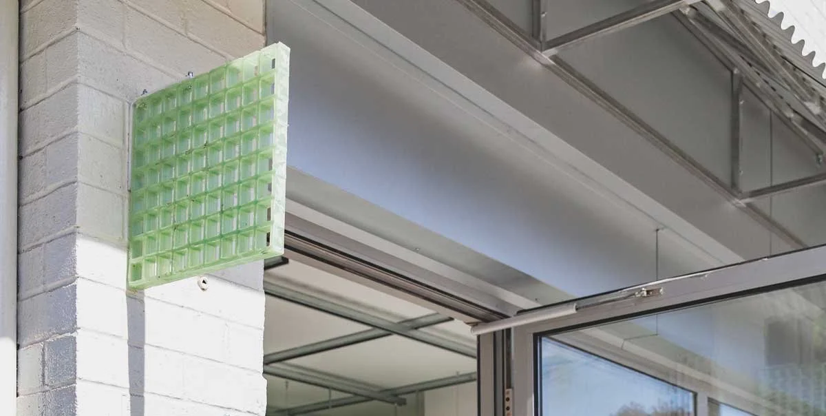 Close-up of a glass window with a white aluminum frame and an exterior wall with white bricks. There is a green plastic ice cube tray attached to the wall near the corner.