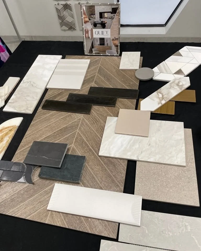 A variety of tiles and samples displayed on a black table, with a mirror and a decorative wall piece in the background.