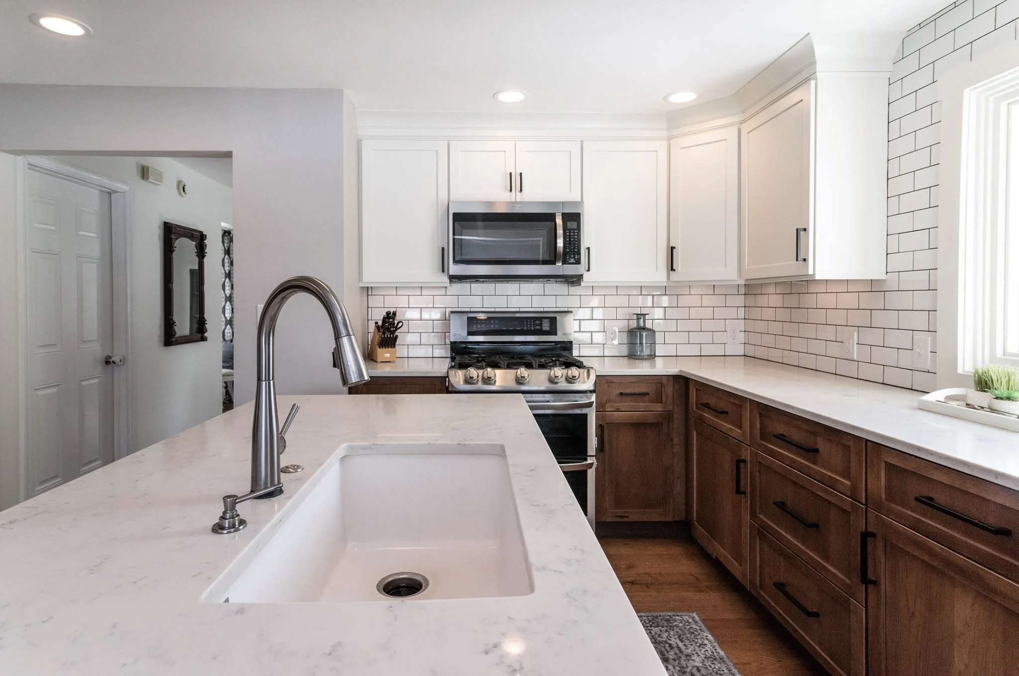 Modern kitchen with white cabinets, stainless steel microwave and stove, white subway tile backsplash, white countertop, and wooden lower cabinets.