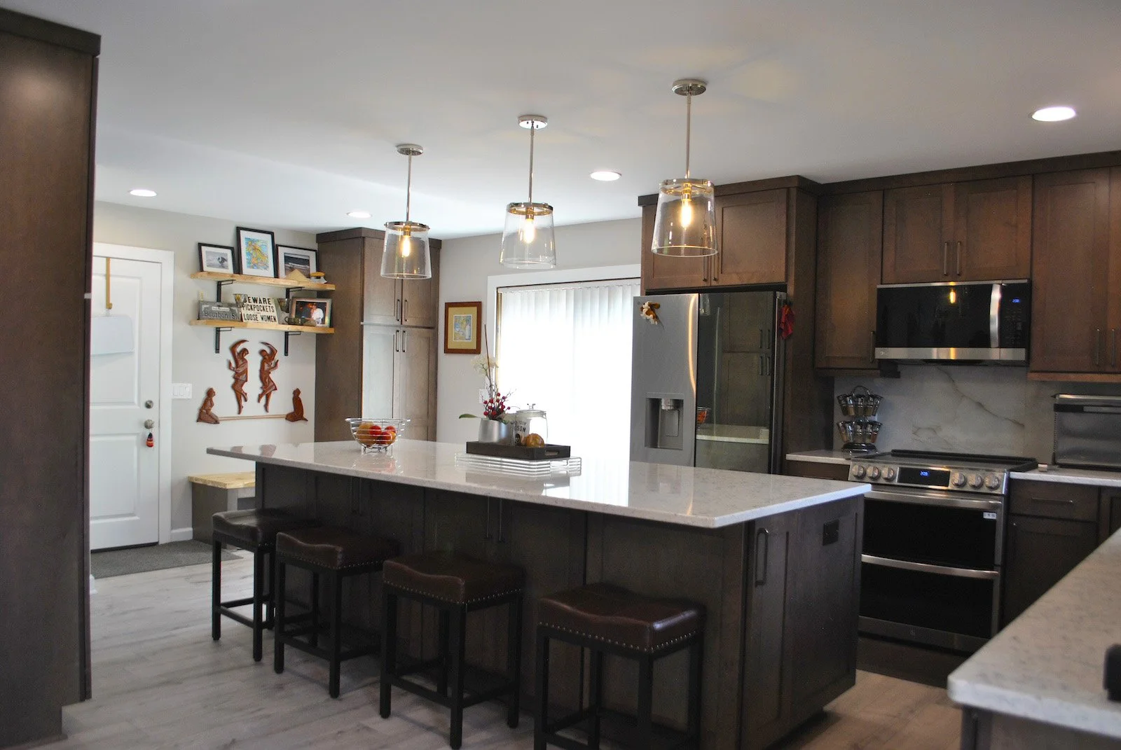 Modern kitchen with dark wood cabinets, white countertops, and stainless steel appliances, including a microwave and refrigerator, illuminated by pendant lights and recessed ceiling lights.