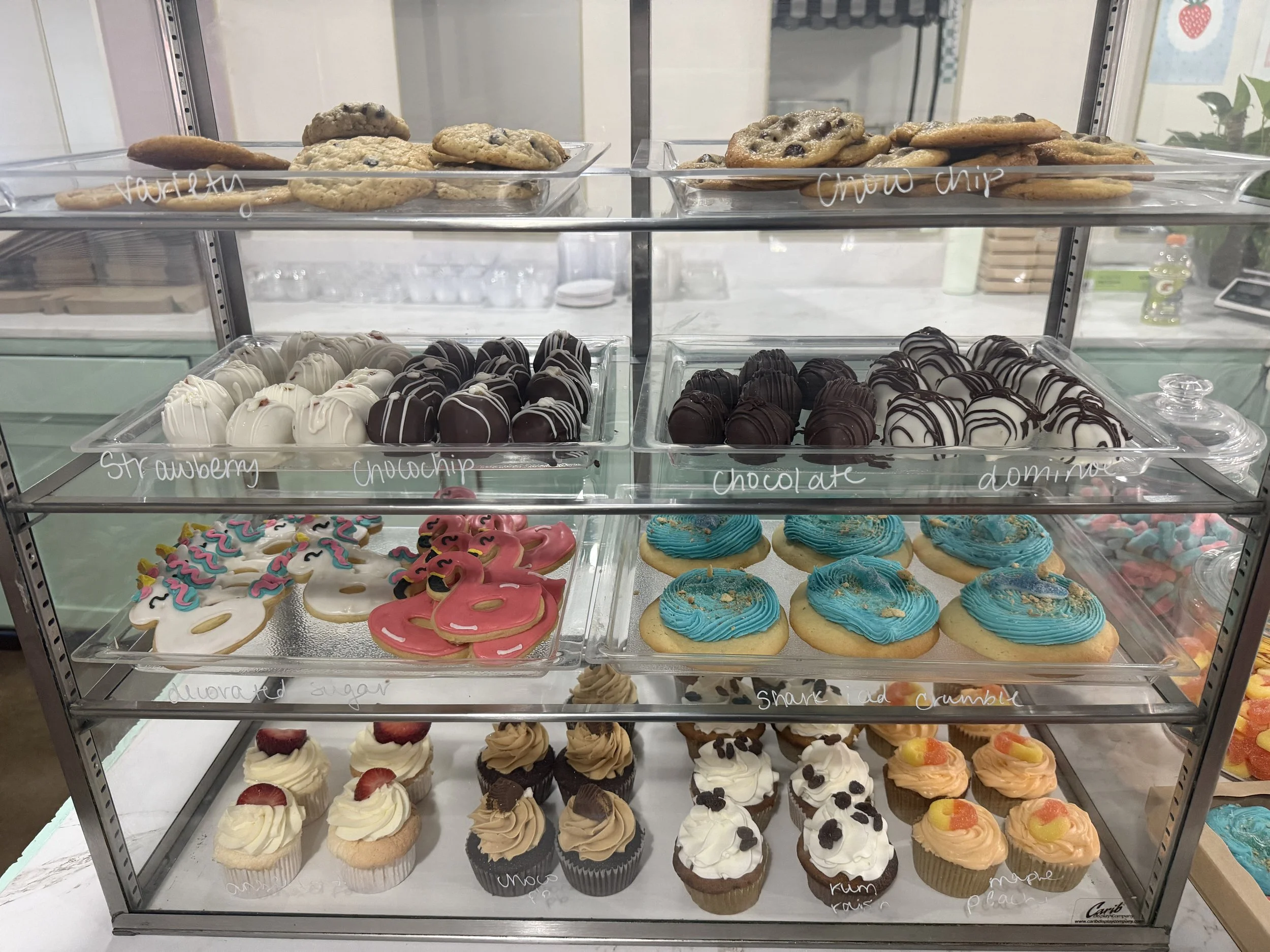 A glass display case with three shelves filled with various cookies, cupcakes, and decorated sugar cookies.