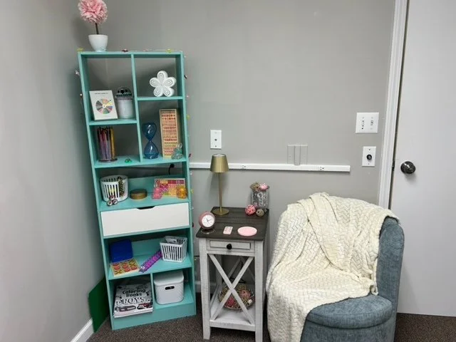 View of a cozy corner at Hopeful Healing Therapy in Kansas City with a blue bookshelf, a small white side table, and a gray armchair with a beige blanket.