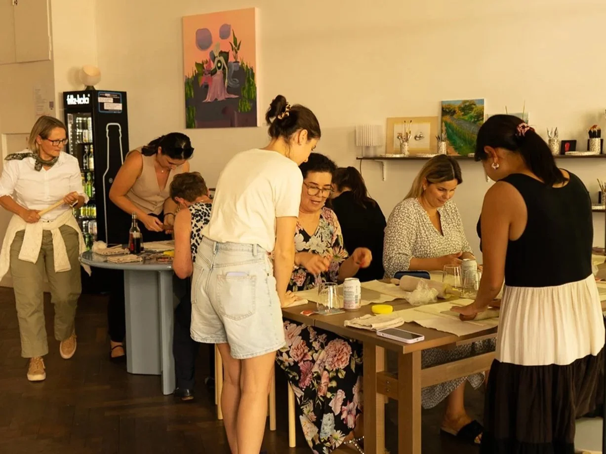 Group of women gathering around a table in an art studio or workshop, engaging in arts and crafts activities.