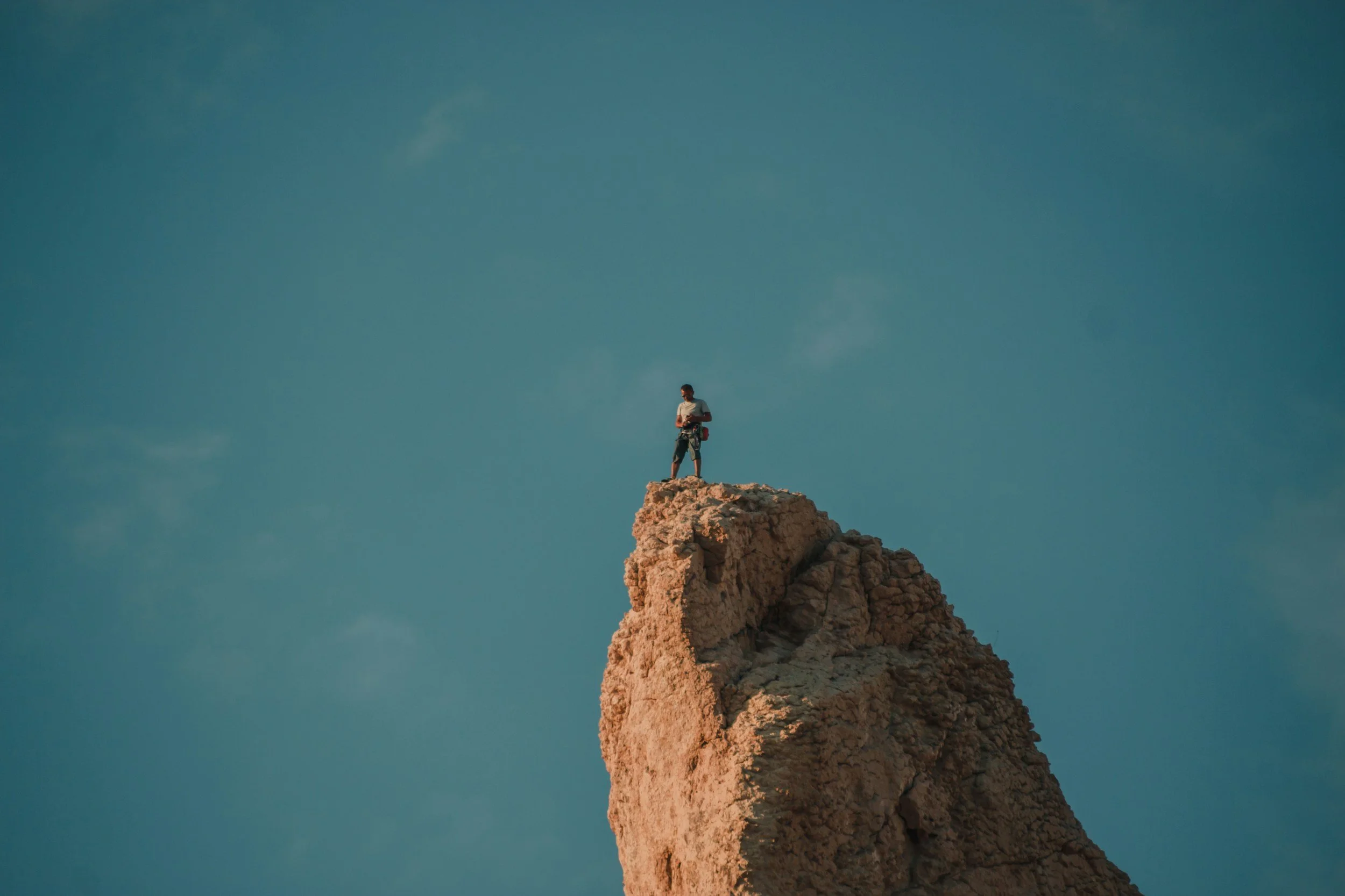 Person standing on top of a large rock formation against a clear sky.