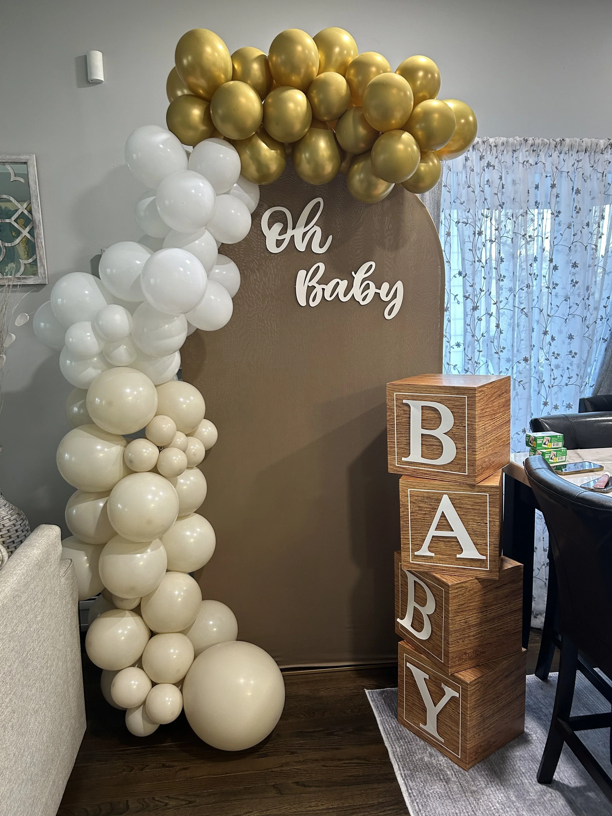 Decorative balloon arrangement with gold and white balloons, a backdrop with the words "Oh Baby" and wooden blocks spelling out "BABY".