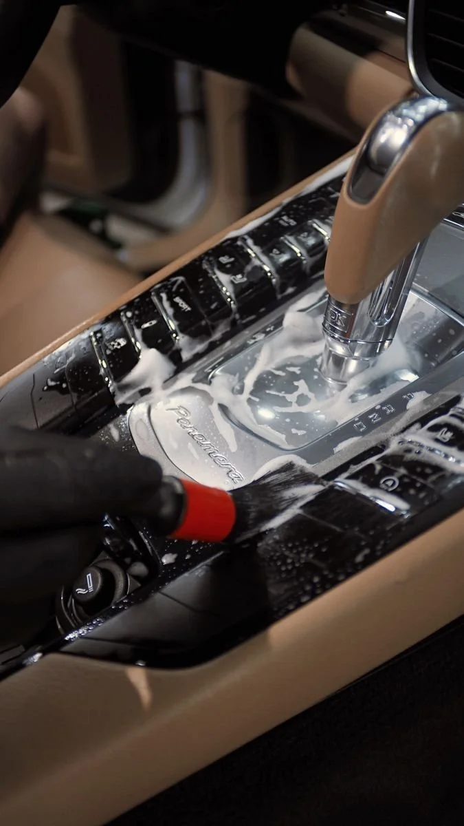 Close-up of a car's gear shift with foam and a cleaning brush being used to clean the area.