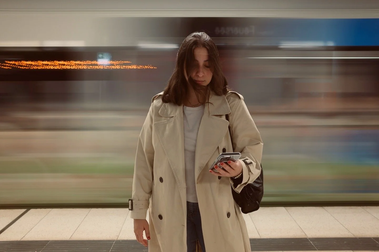 Frau steht an einer Bahnsteig, schaut auf ihr Smartphone.