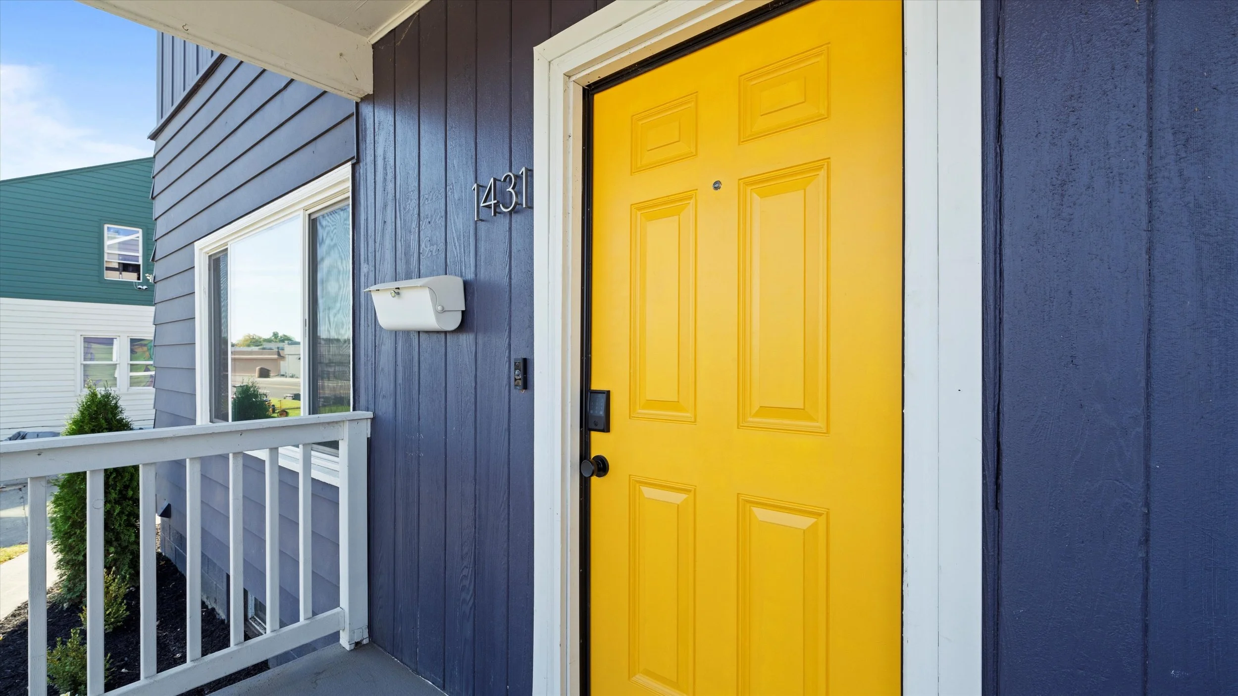Close-up of a yellow front door with a doorknob and electronic lock, situated on a blue house with white trim, house number 143, and a white mailbox outside.