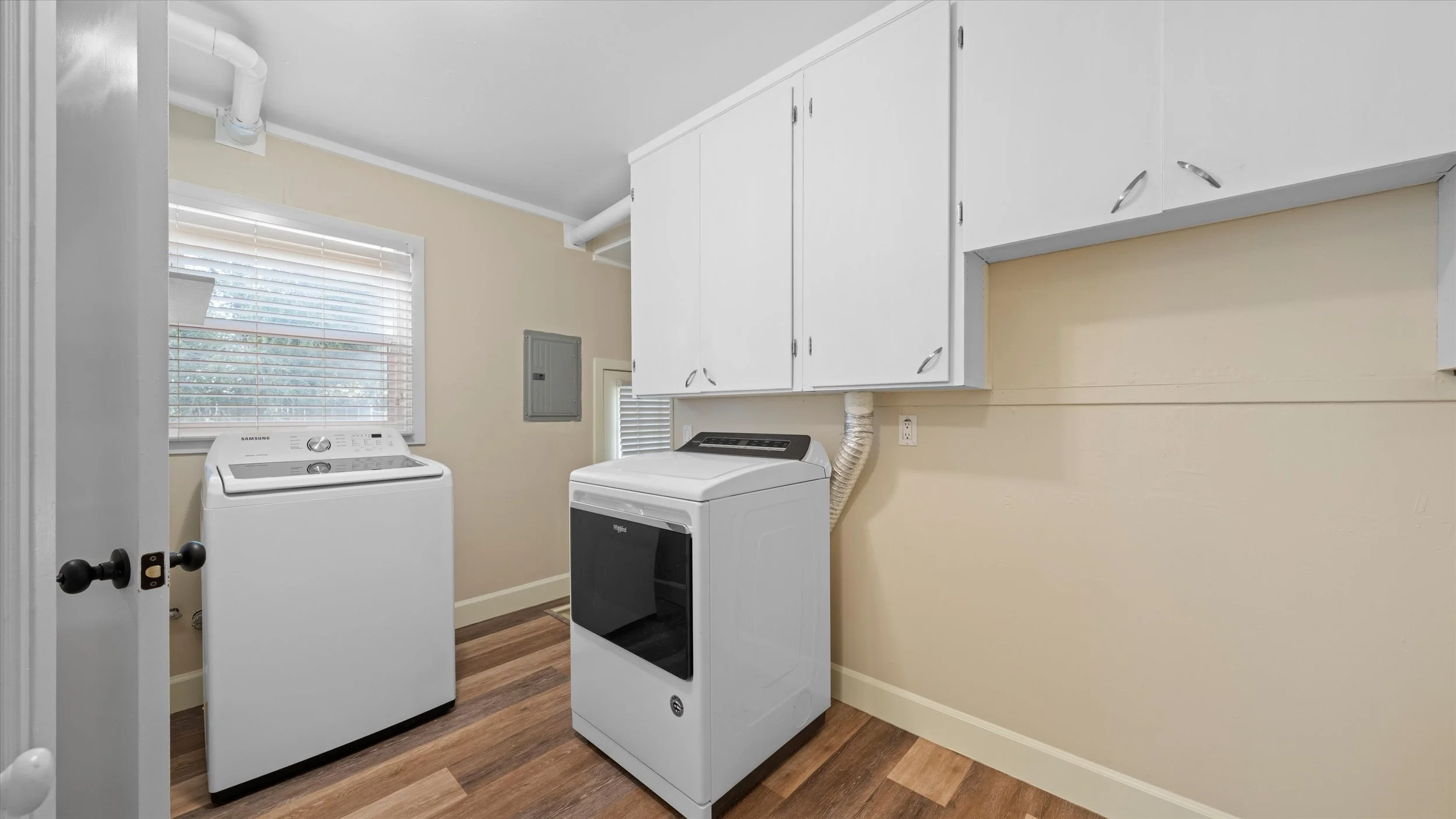Laundry room with a window, a white washing machine, a white dryer, and white cabinetry on the wall.
