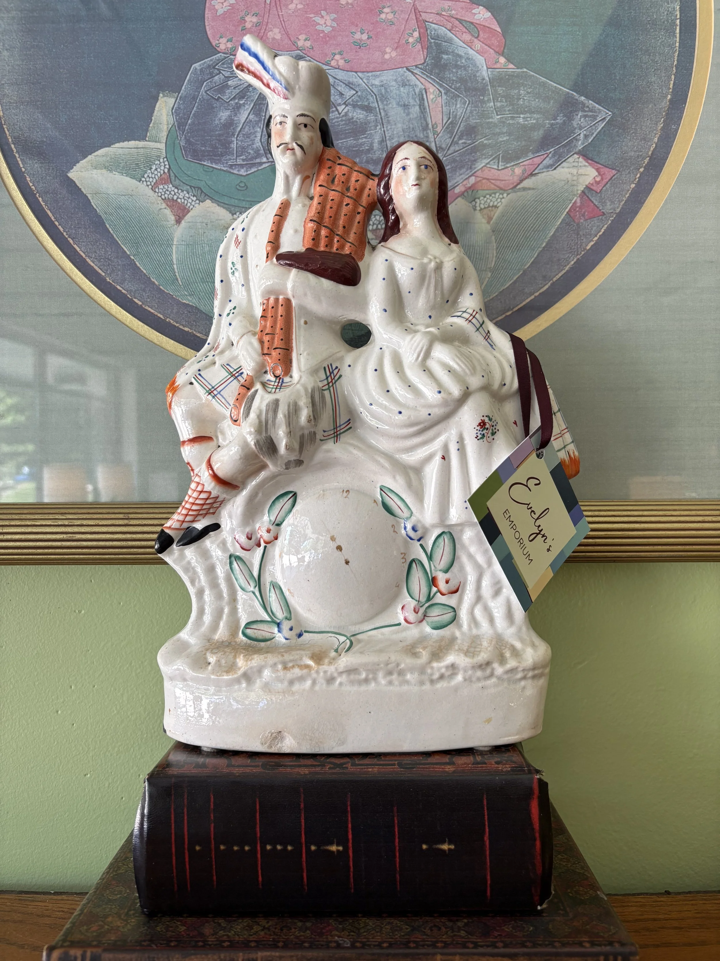 Antique Staffordshire flatback Highland Couple figurine made between 1840 and 1900, Evelyn's Emporium Saint Paul. The man wearing a red headdress and an orange scarf, and the woman dressed in white with red and green accents.