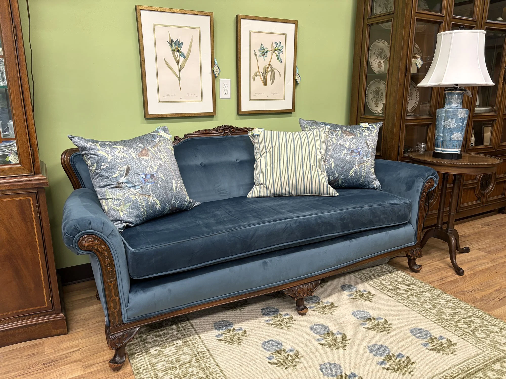 Antique Victorian sofa in blue velvet styled with botanical and striped throw pillows against a green wall, Evelyn's Emporium Saint Paul.