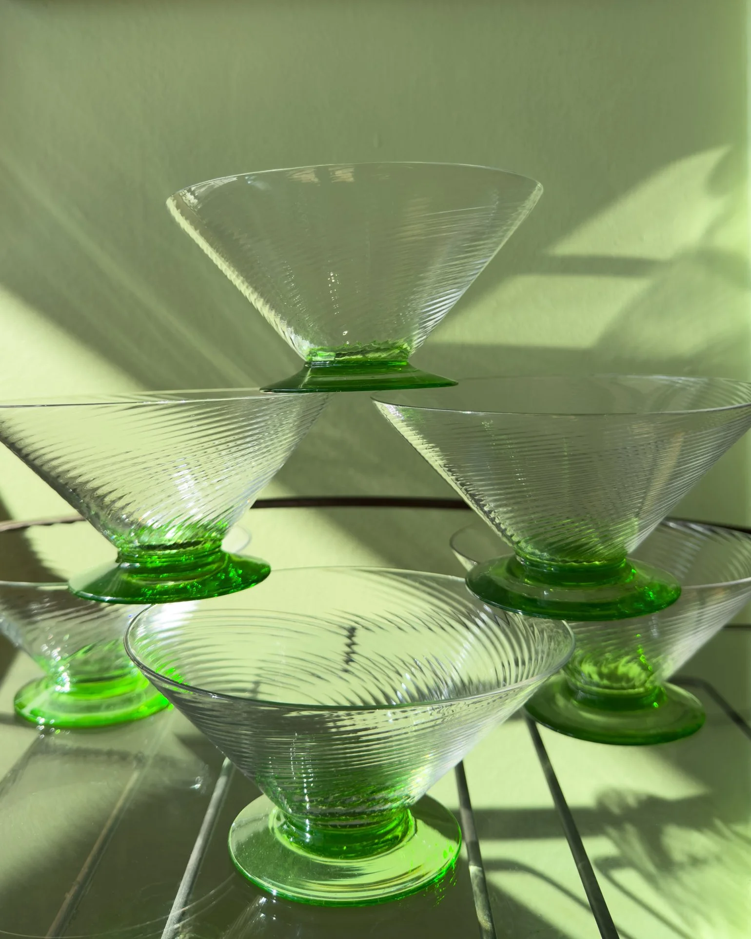 Set of six turn-of-the-century green uranium glass footed sherbet dishes, Evelyn's Emporium in Saint Paul, MN. They are stacked one on top of the other, have textured surfaces, and are casting shadows on a reflective surface.