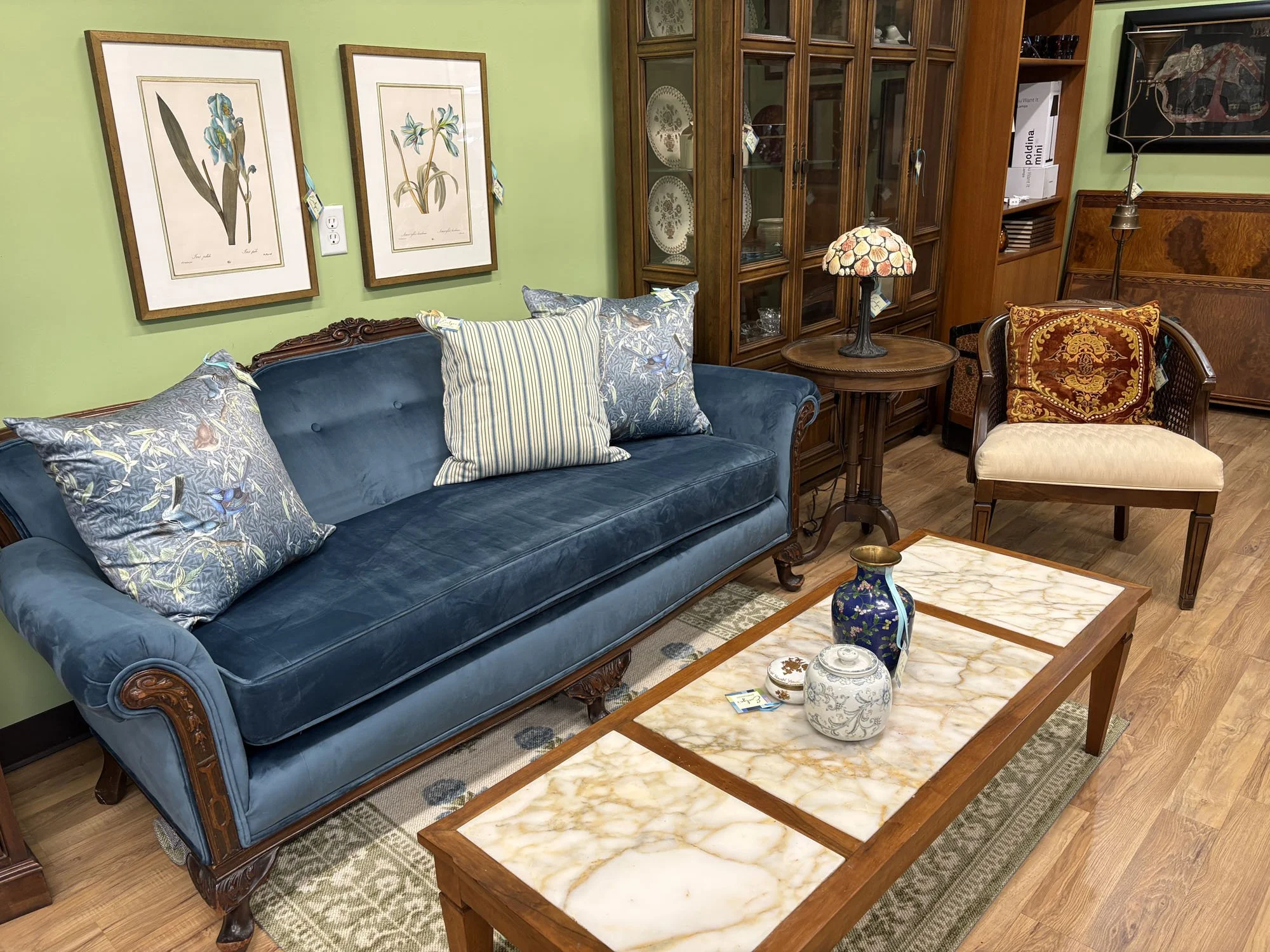 Antique Victorian sofa reupholstered in blue velvet, shown in a full room setting with a marble-top coffee table and botanical prints on the wall, Evelyn's Emporium Saint Paul.