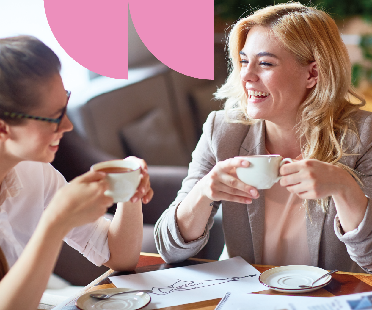 Two women sitting at a table, smiling and enjoying coffee together, engaging in conversation.