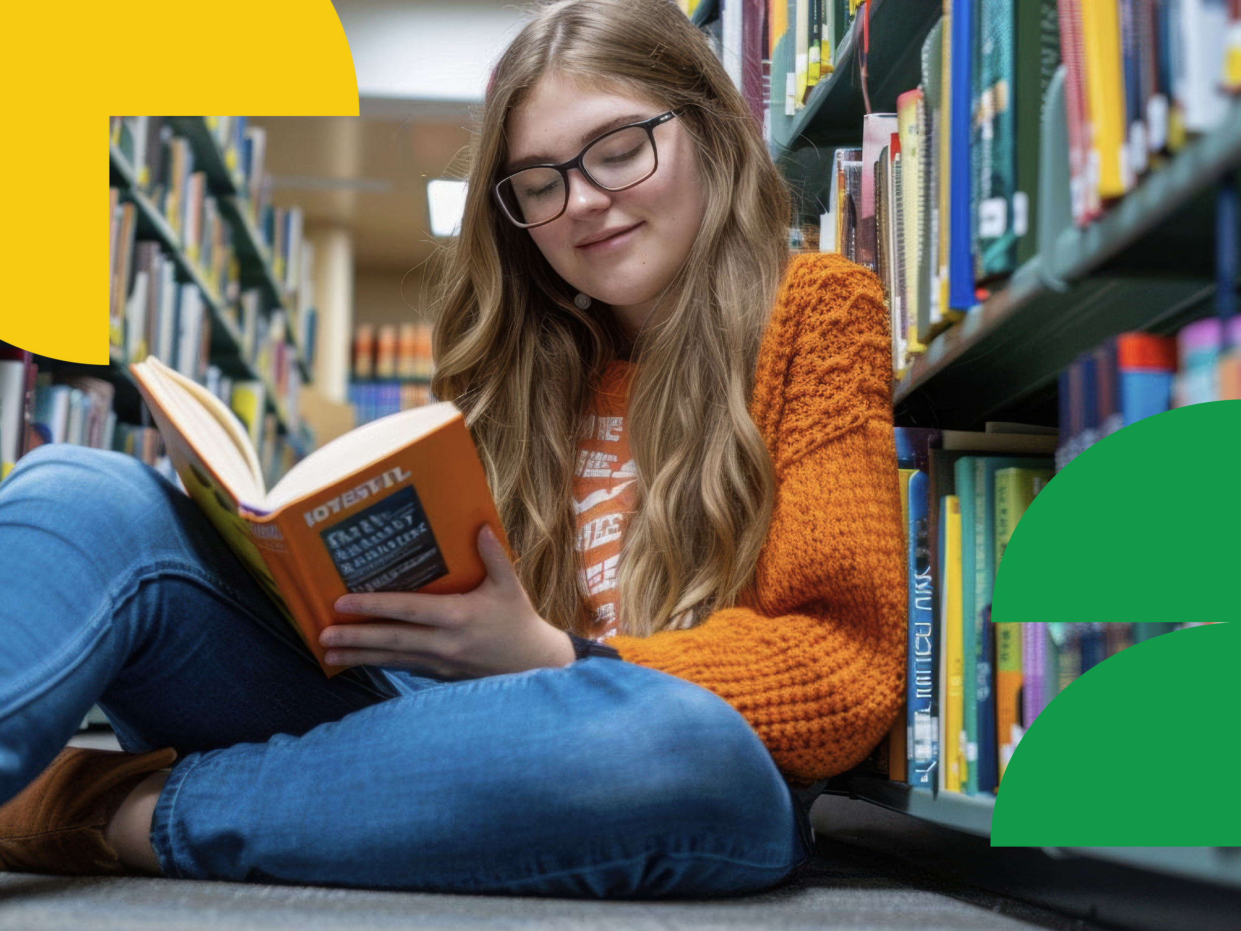 A young woman with long curly hair wearing glasses, an orange sweater, and blue jeans, sitting on the floor in a library, reading a book.