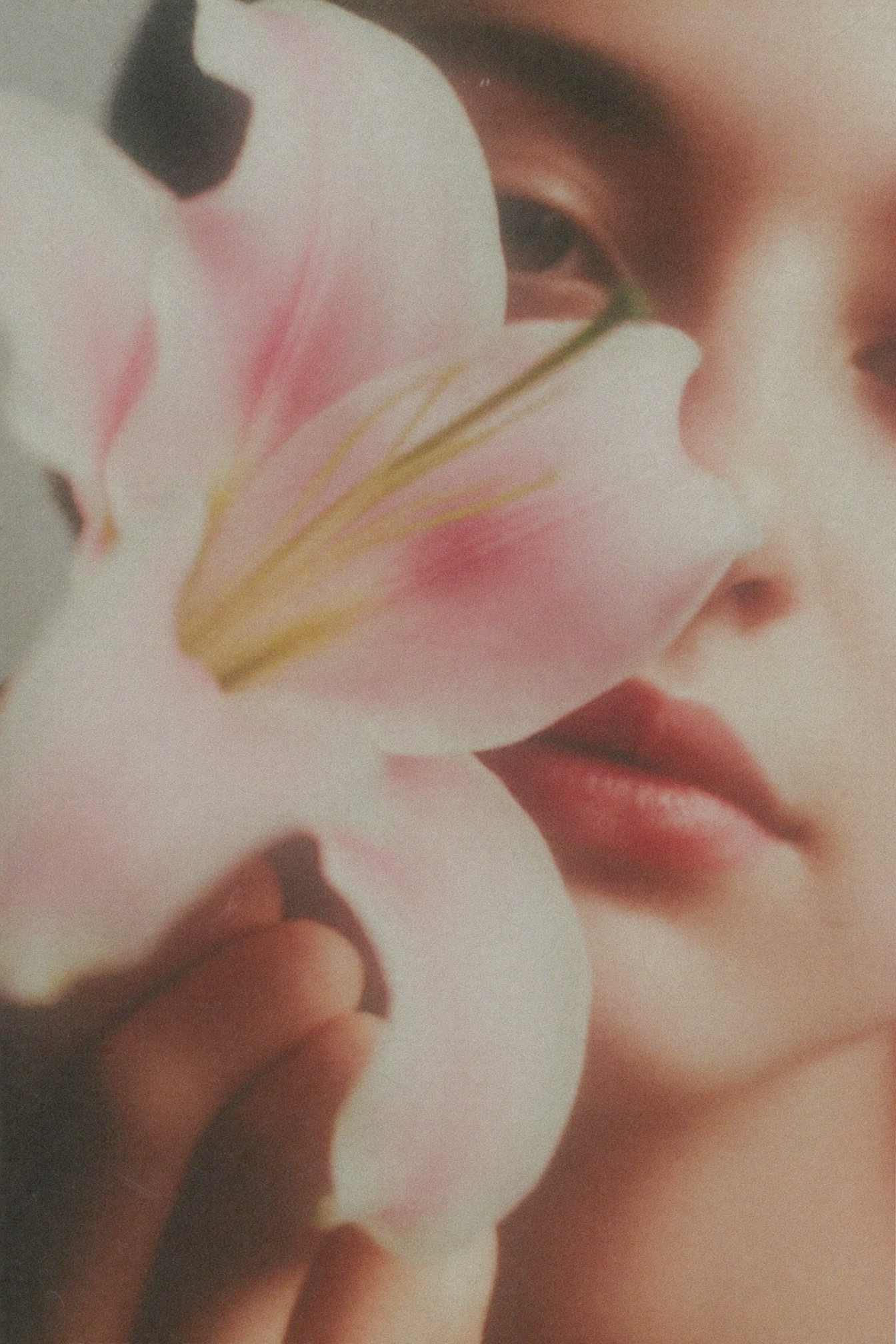 Close-up of a person's face with a pink lily flower partially covering the face.