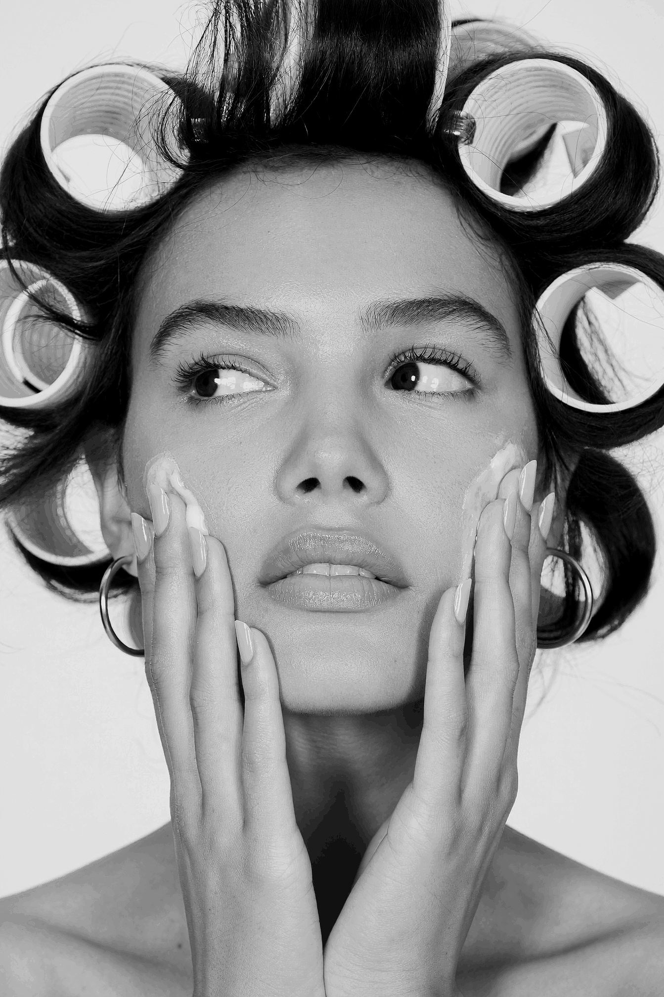 A woman with dark hair in hair rollers, touching her face with her hands, in black and white.
