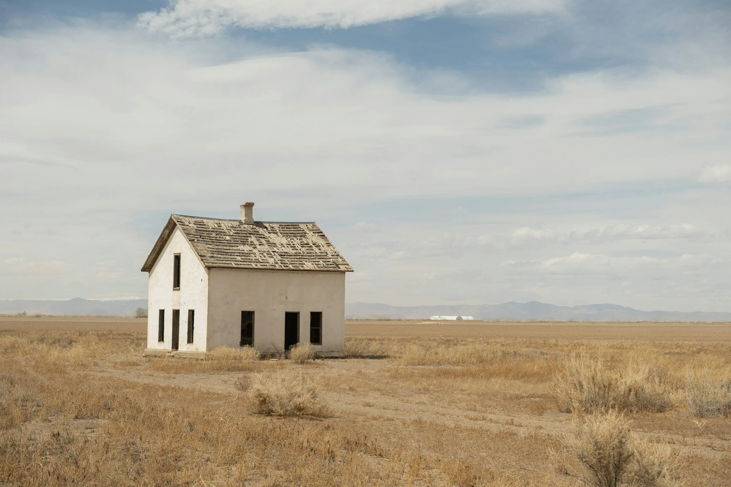 abandoned white farm house in dusty barren brown field