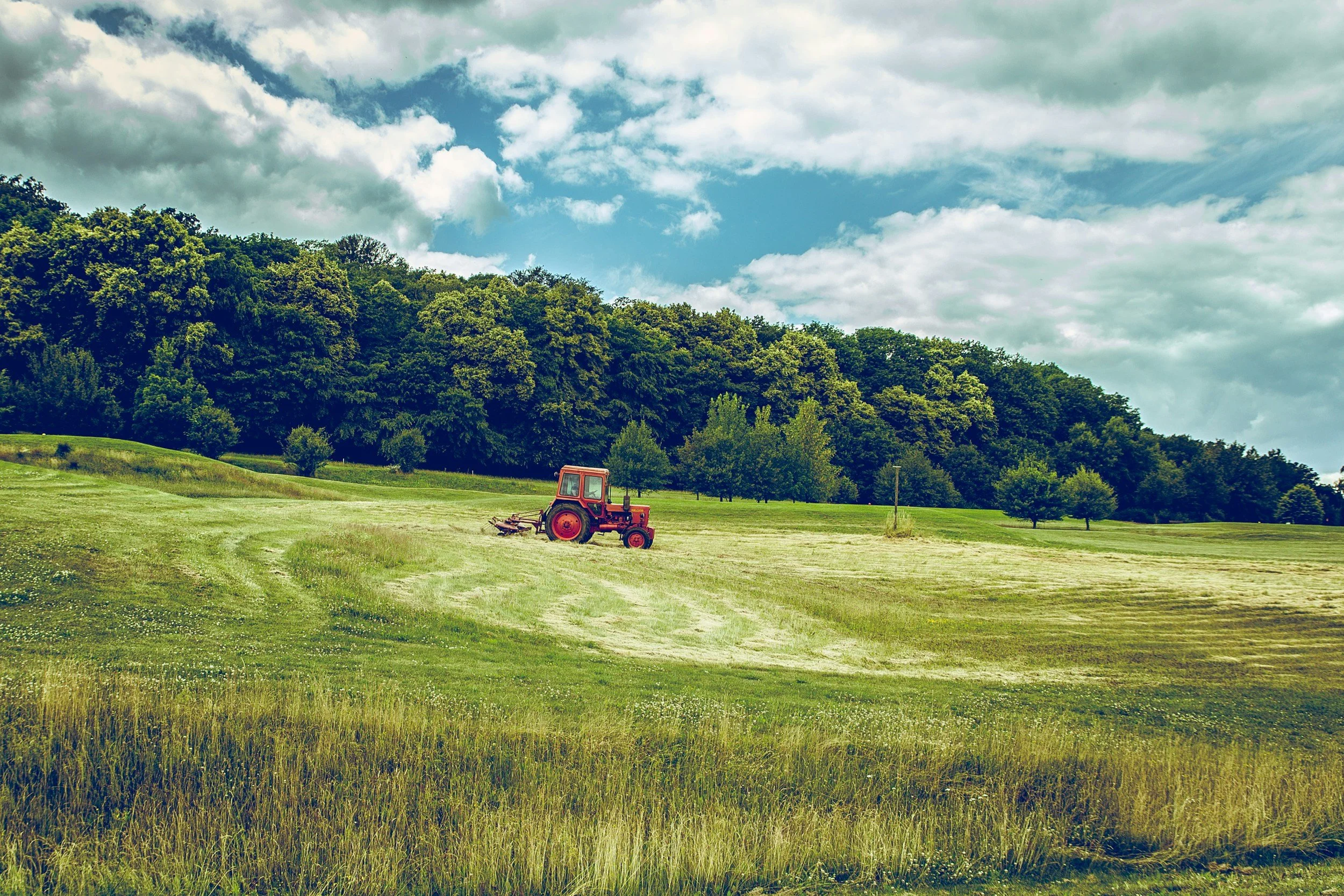 red tractor mowing field with trees and clouds in background