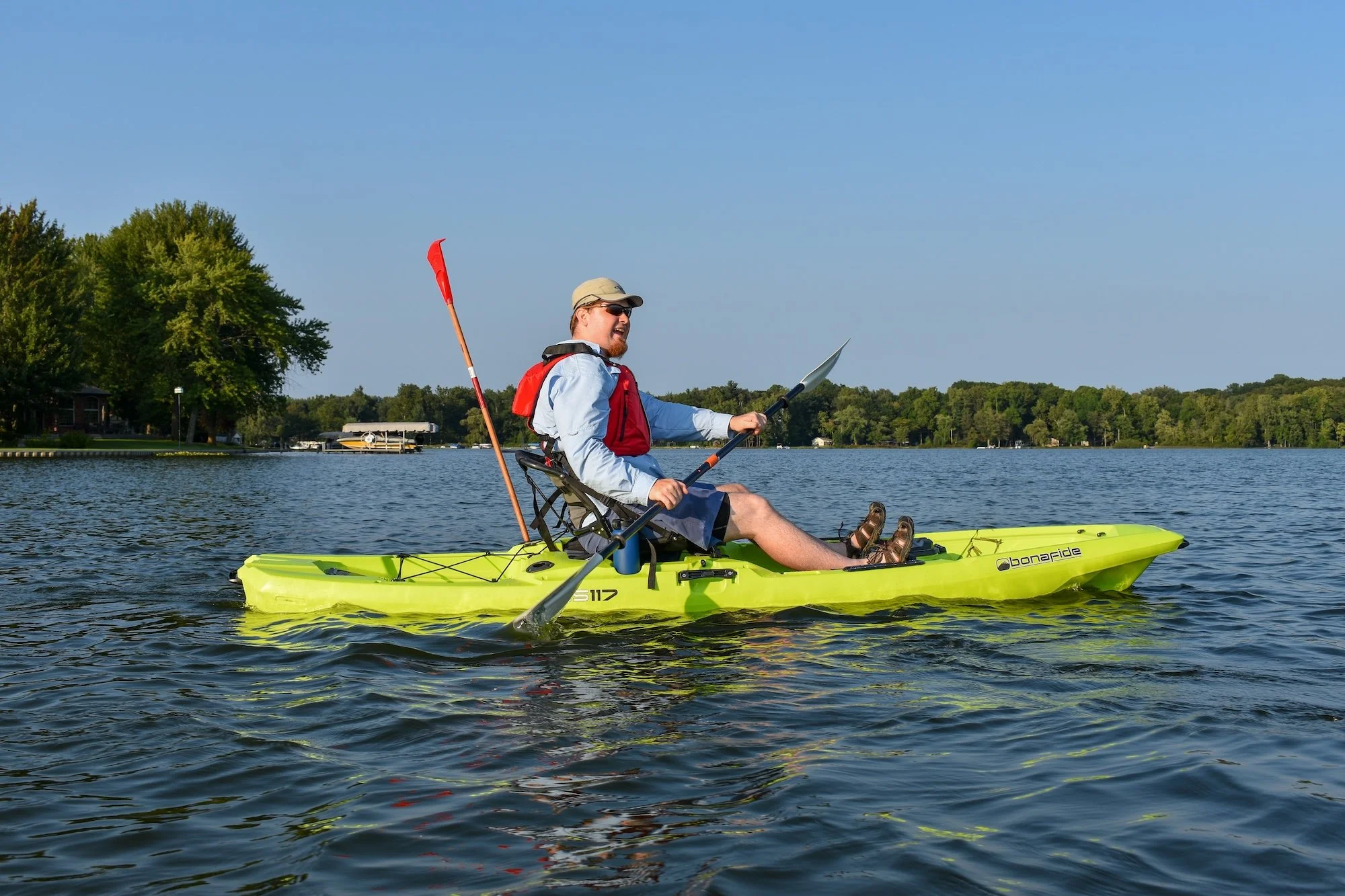 male kayaker in red lifejacket paddles on lake using bright pale green kayak
