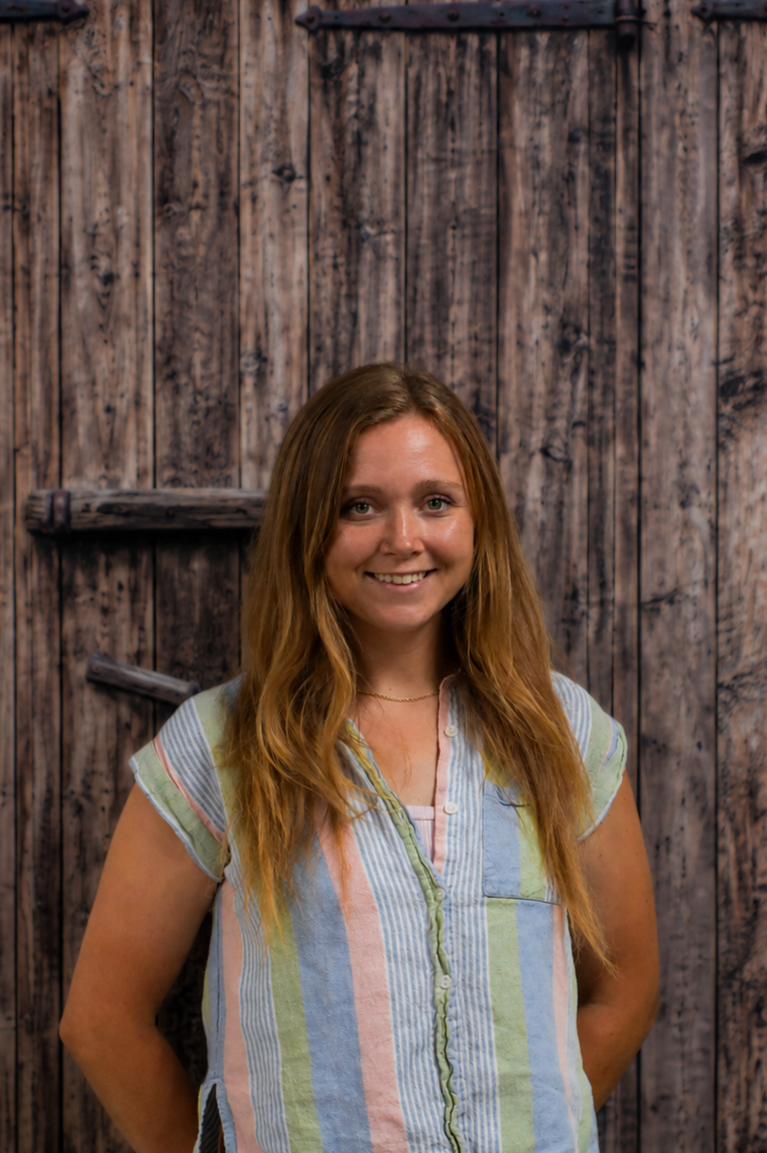 woman smiling for portrait wearing a blue pink and green vertical stiped linen short sleeve shirt in front of a digitally added wood background