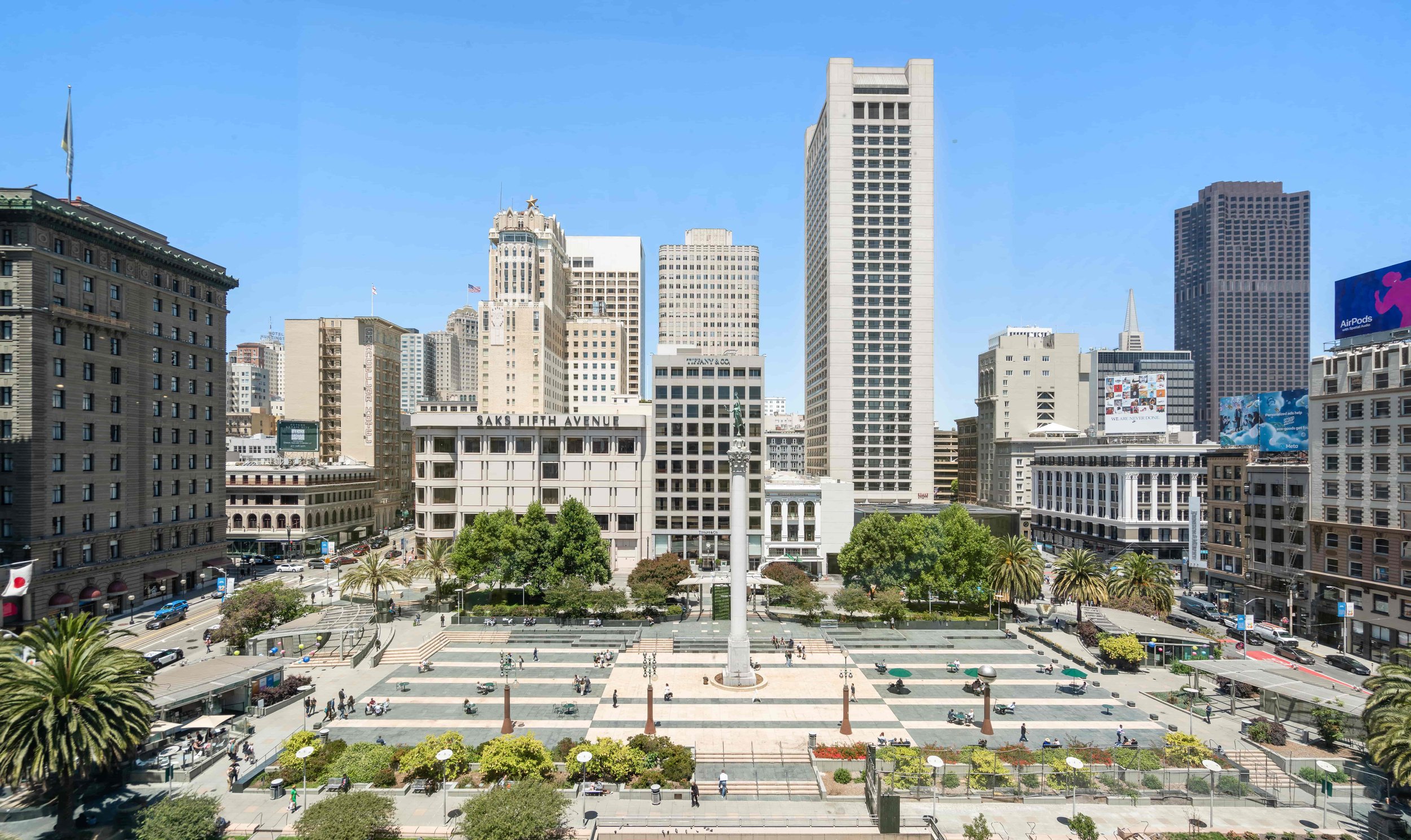 View of Union Square in San Francisco with tall skyscrapers, a central statue, a public square, and people walking and relaxing in the area.