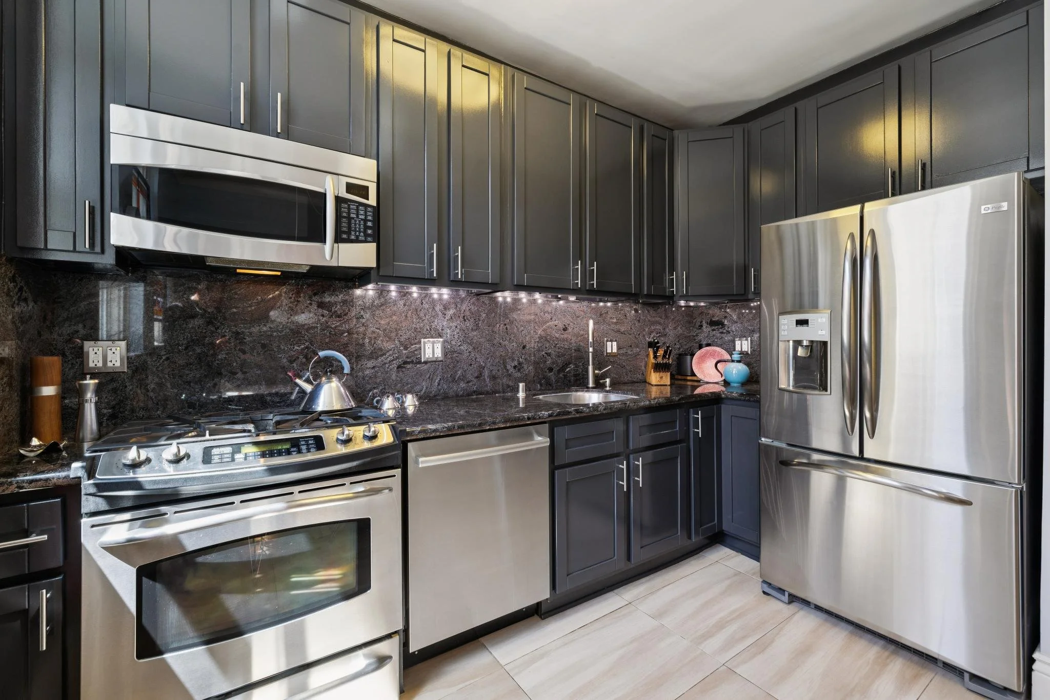 Modern kitchen with black cabinets, stainless steel appliances, black granite countertops, and tiled flooring.