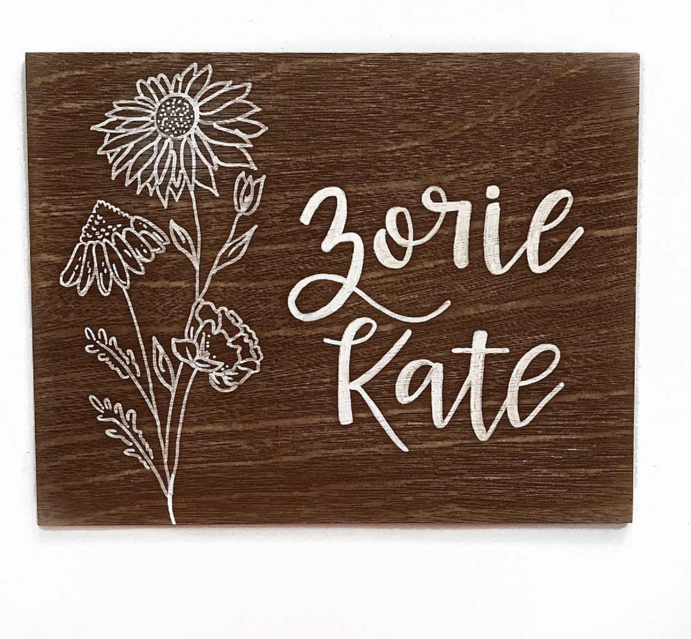 Wooden sign with white floral designs and the names "Zorie & Kate" written in a cursive font.