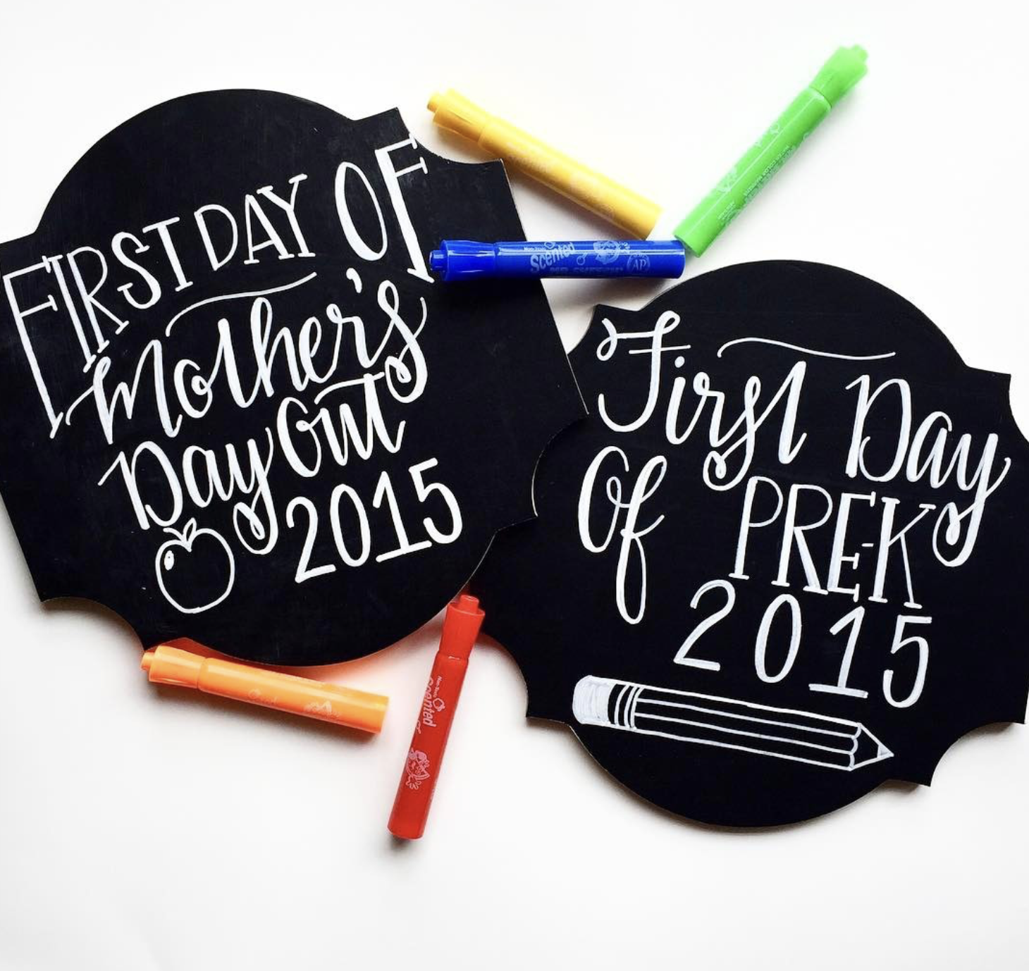 Black chalkboards with white handwritten text saying "First Day of Mothers Day Out 2015" and "First Day of PreK 2015," surrounded by colorful chalks on a white background.