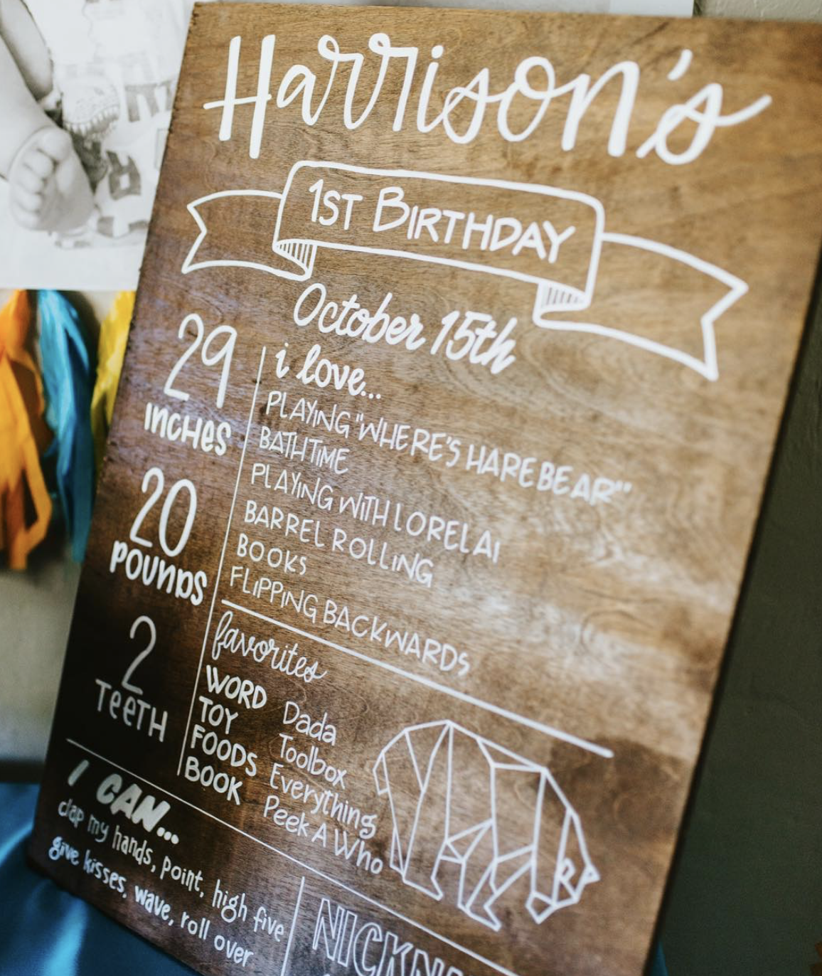A wooden sign celebrating a child's first birthday, with details about the child's age, height, weight, favorite things, and a drawing of an elephant.