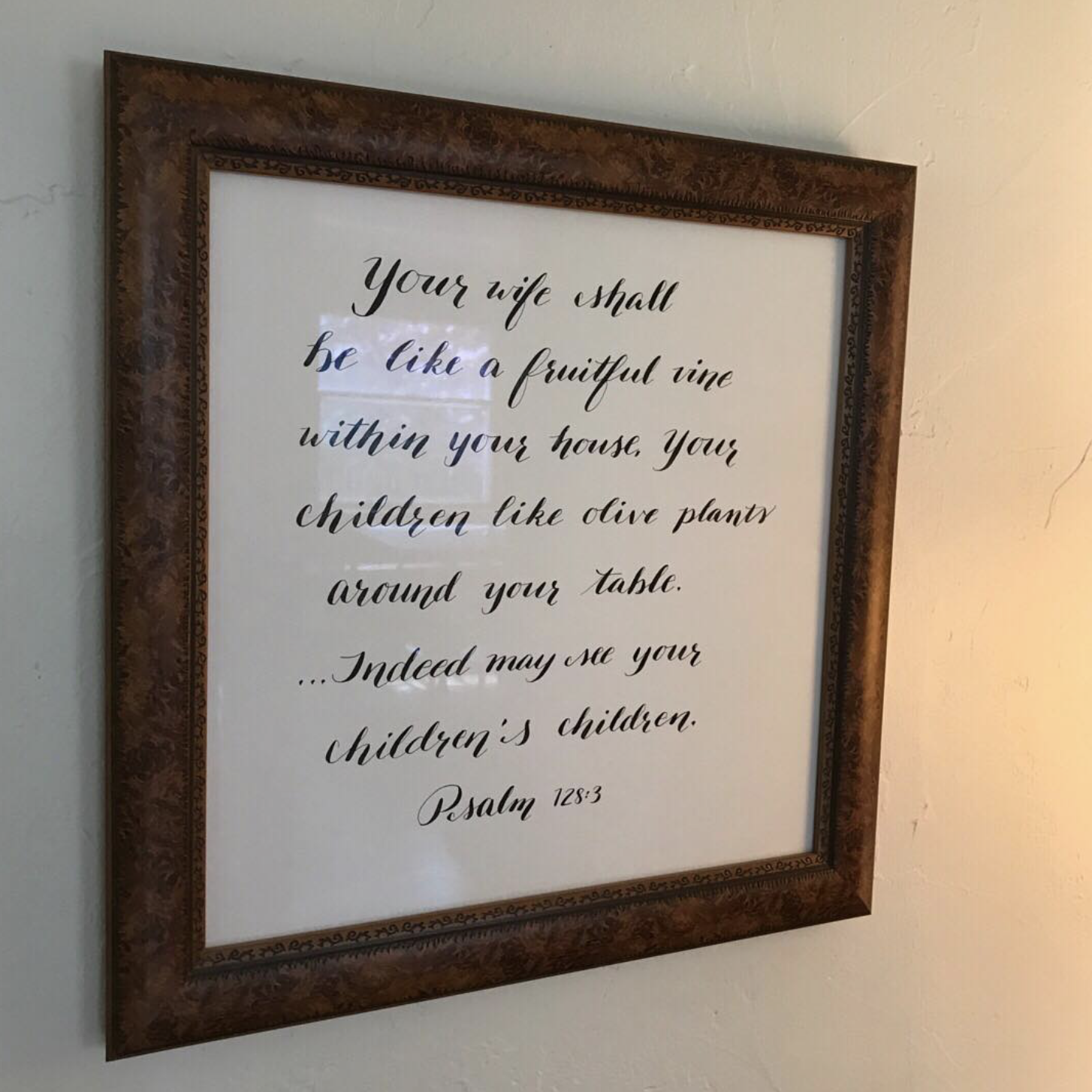 A framed print of a biblical quote from Psalm 128:3 about a wife being like a fruitful vine within your house.