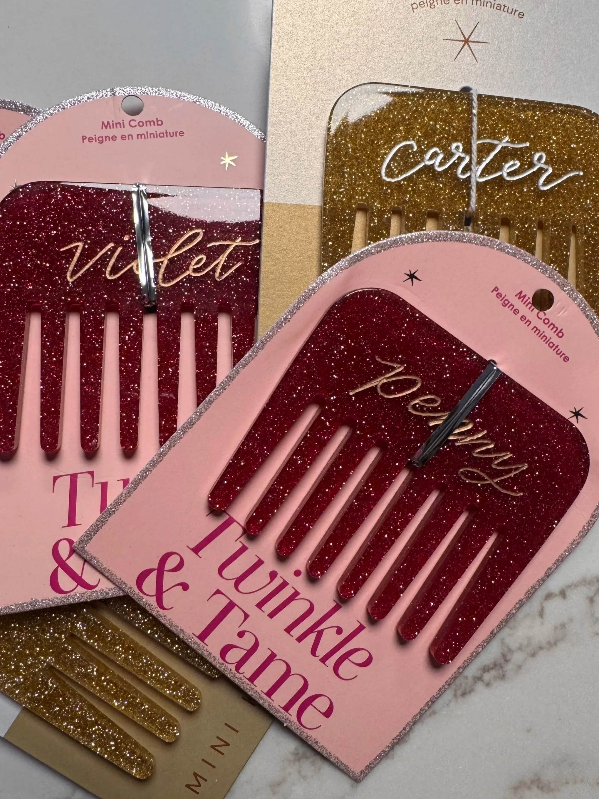 Close-up of pink and gold glitter hair combs with the words 'vibe' and 'corter' written on them, displayed on glittery packaging.