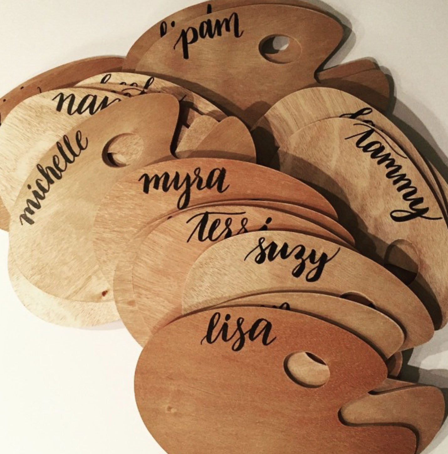 Wooden tags with black cursive lettering displaying names such as Lisa, Suzy, Myra, Tess, and Pam, arranged overlapping each other.