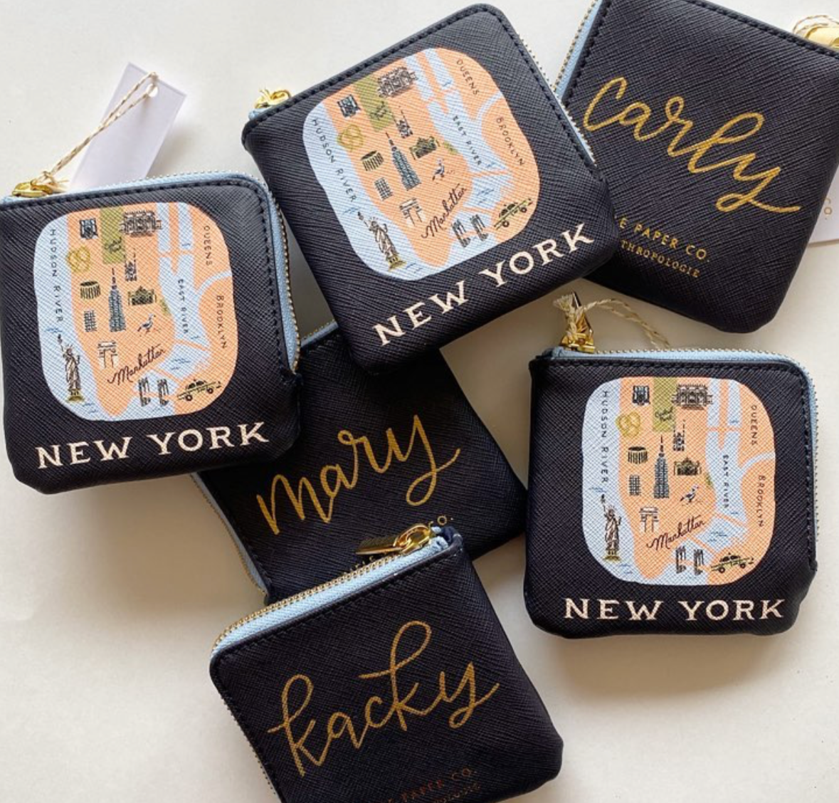 Collection of small black pouches with gold and yellow text, some featuring a map of New York City and others with city names 'New York,' 'Marry,' and 'Kacky'.