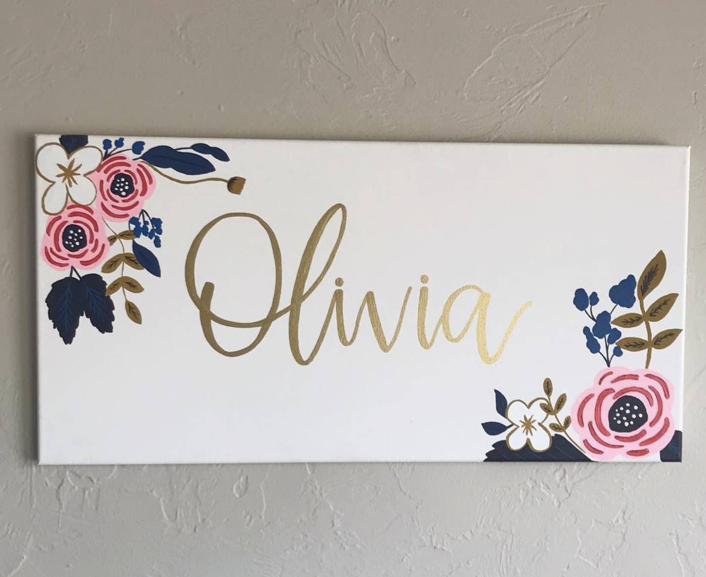 Decorative wall art with the name "Olivia" in gold script, surrounded by floral illustrations in pink, white, blue, and gold.