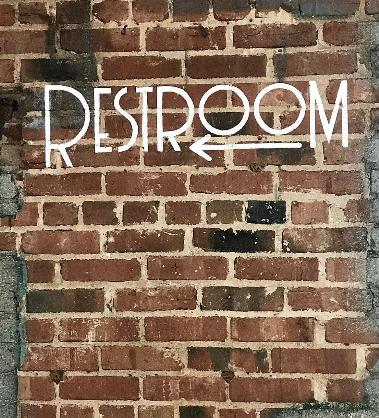 A brick wall with a white neon sign that reads 'RESTROOM' with an arrow pointing left.