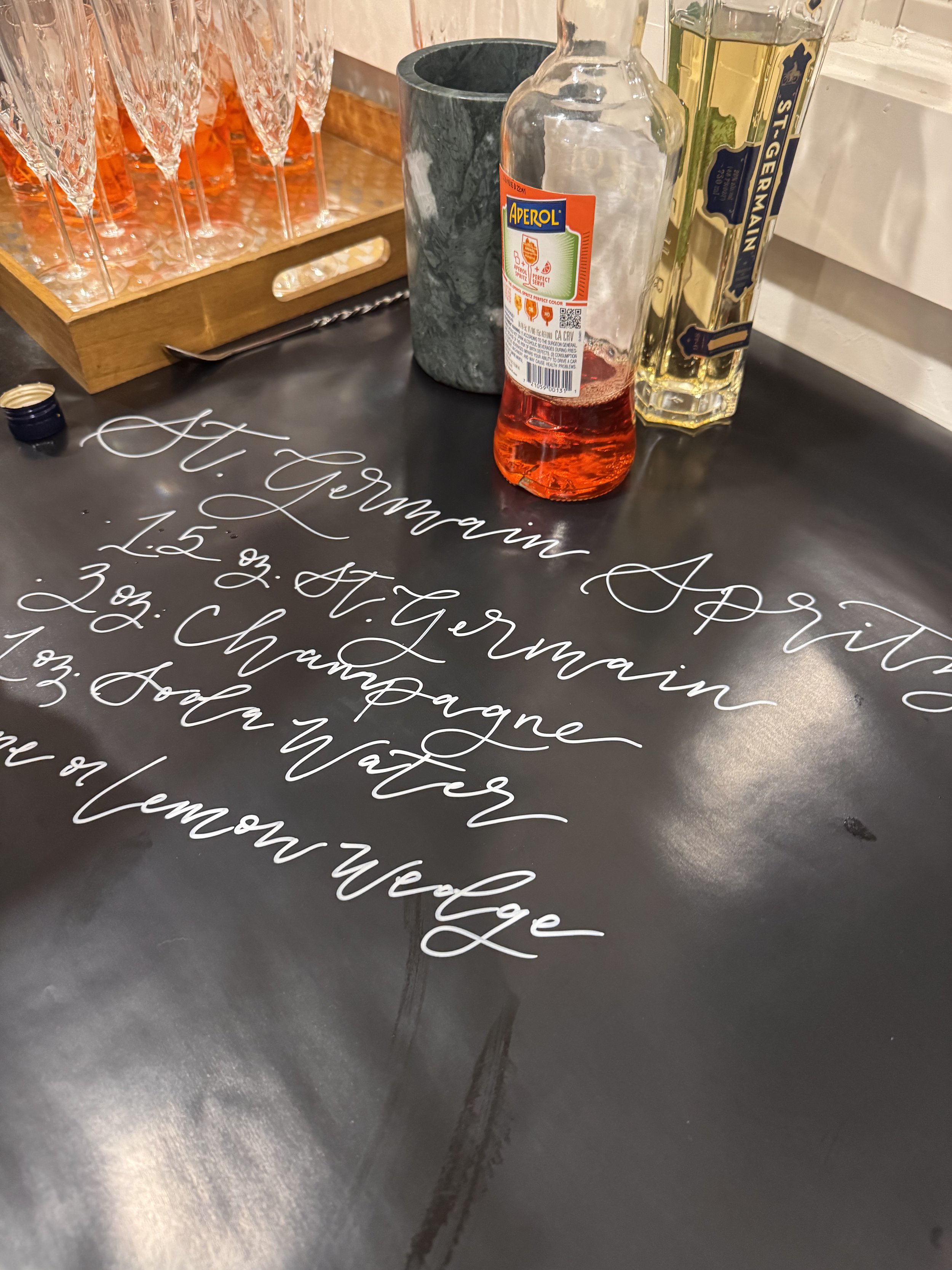 Decorative black surface with white cursive writing listing various wine varieties, including A. Termaine A. P., 1.5 oz, 2 oz, 3 oz, and 1 oz.