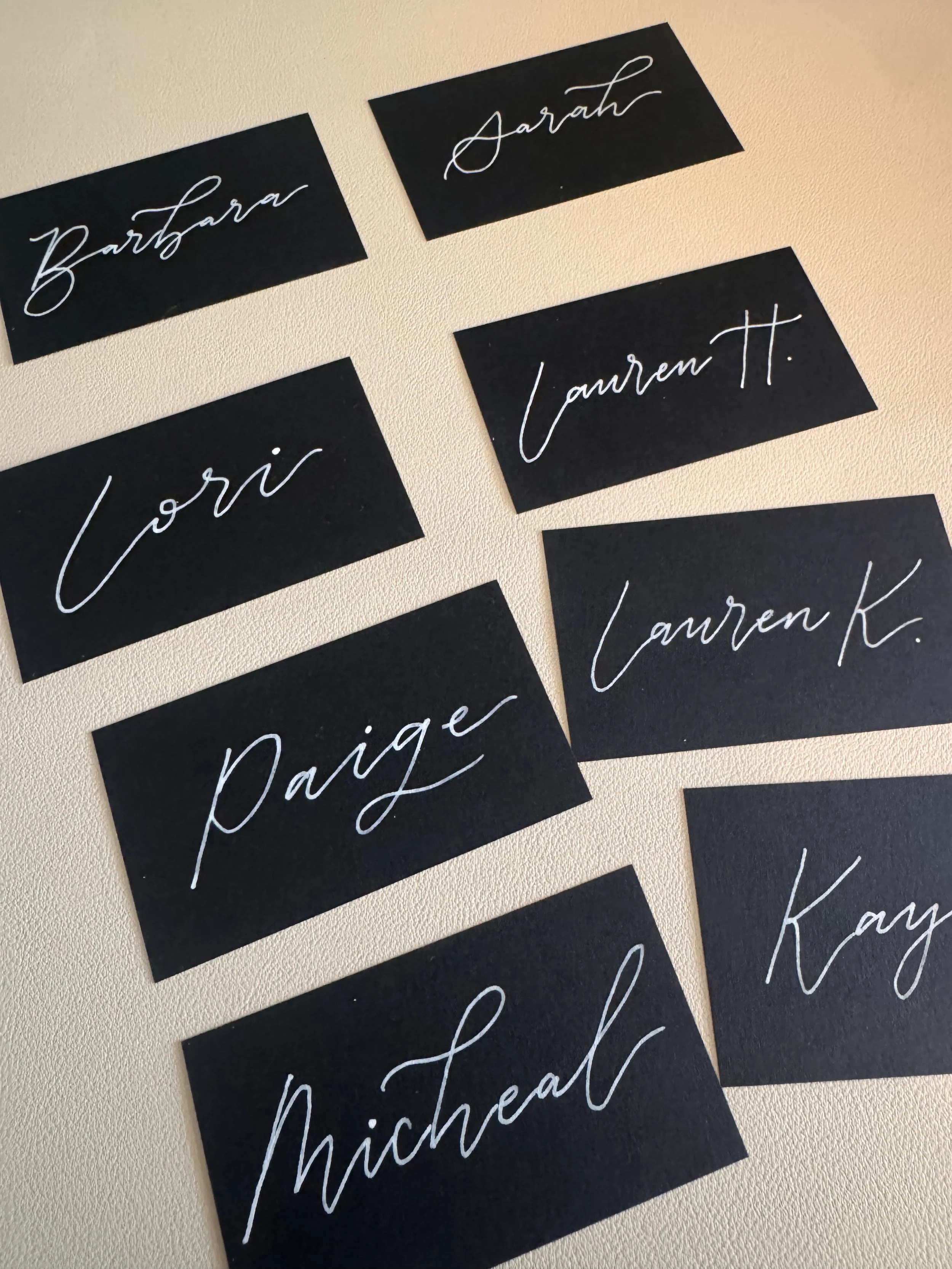 Multiple black rectangular flashcards with white cursive handwriting of names, including 'Barbara', 'Sarah', 'Lauren T.', 'Sori', and 'Nicheal' on a beige surface.